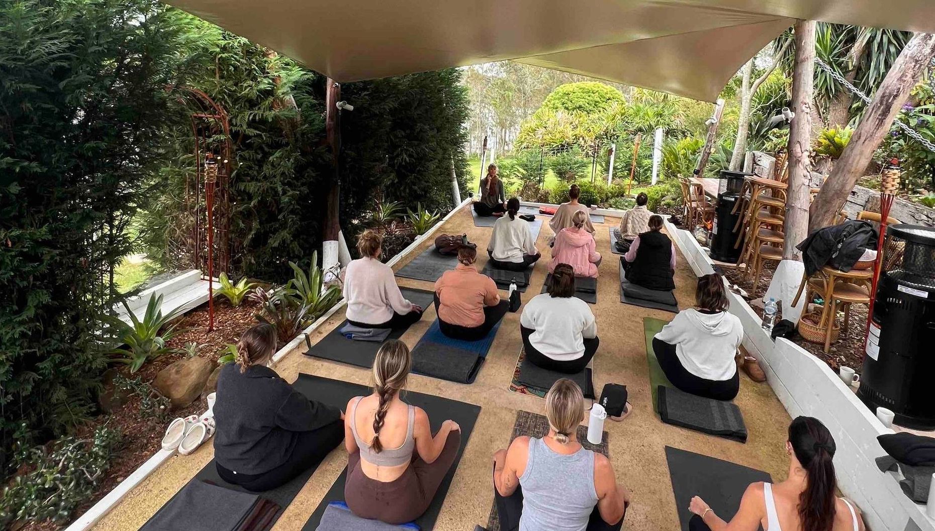 A group of people are sitting on yoga mats under a canopy.