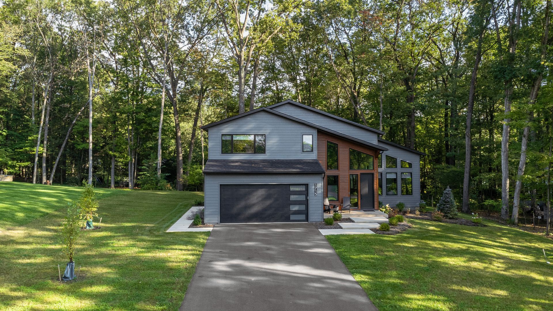 Modern gray house with a garage, large windows, and a driveway surrounded by trees and lawn