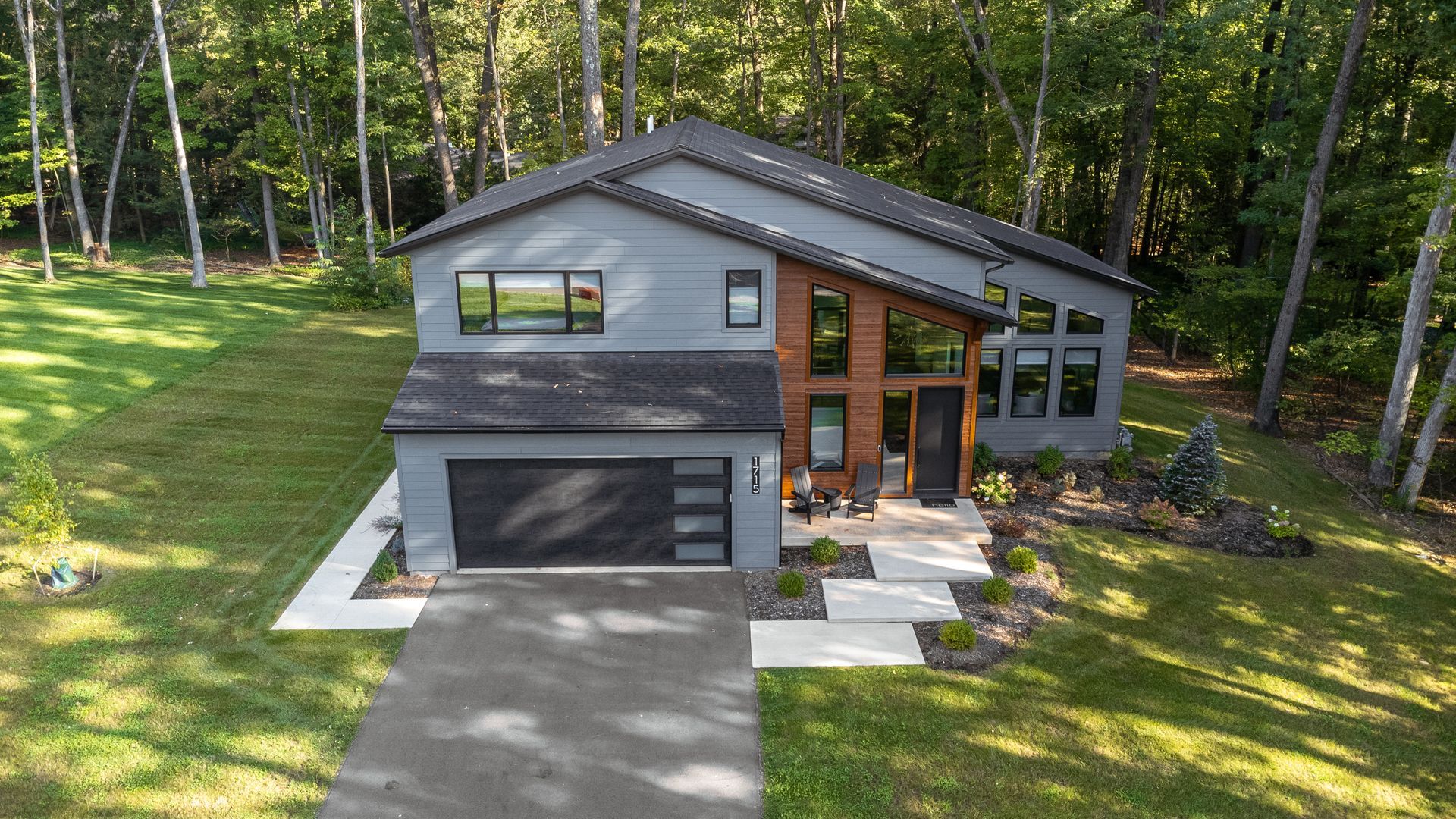 Modern gray two-story house with a garage and front porch, surrounded by trees and a sunlit lawn