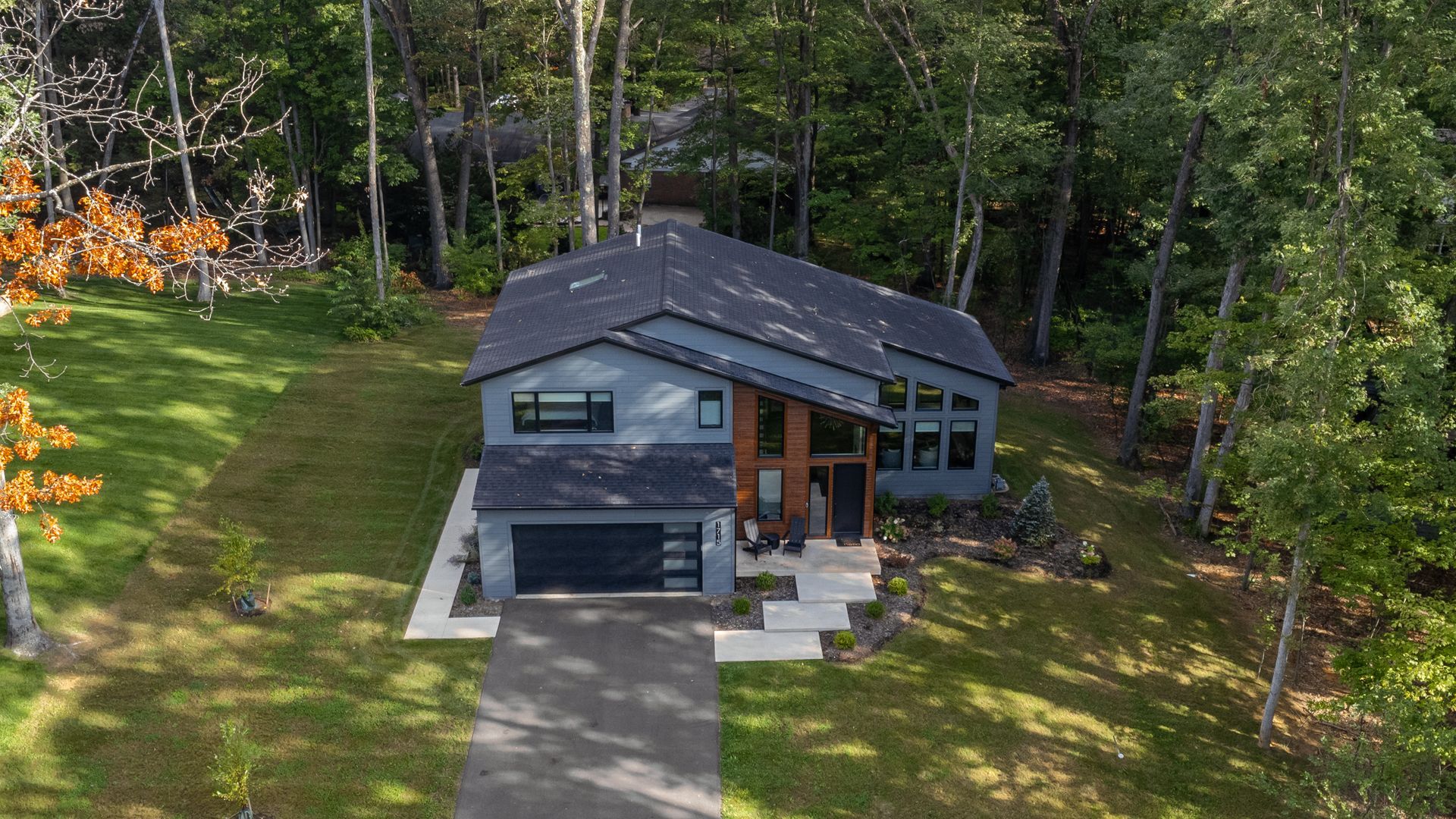 Modern gray house with a dark roof, front driveway, and steps, surrounded by trees and a grassy yard