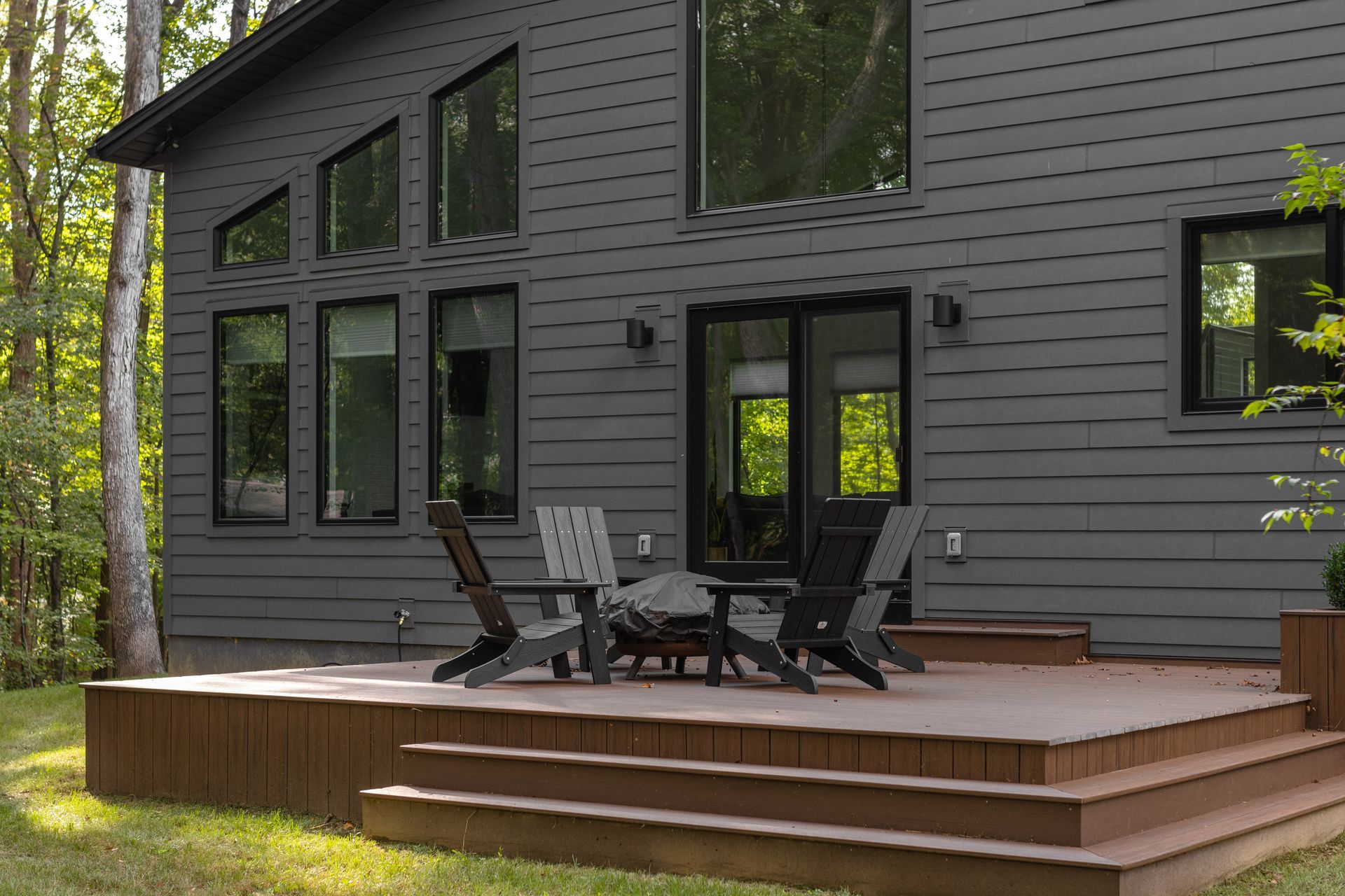 Back deck with outdoor chairs and table beside a gray house with large windows