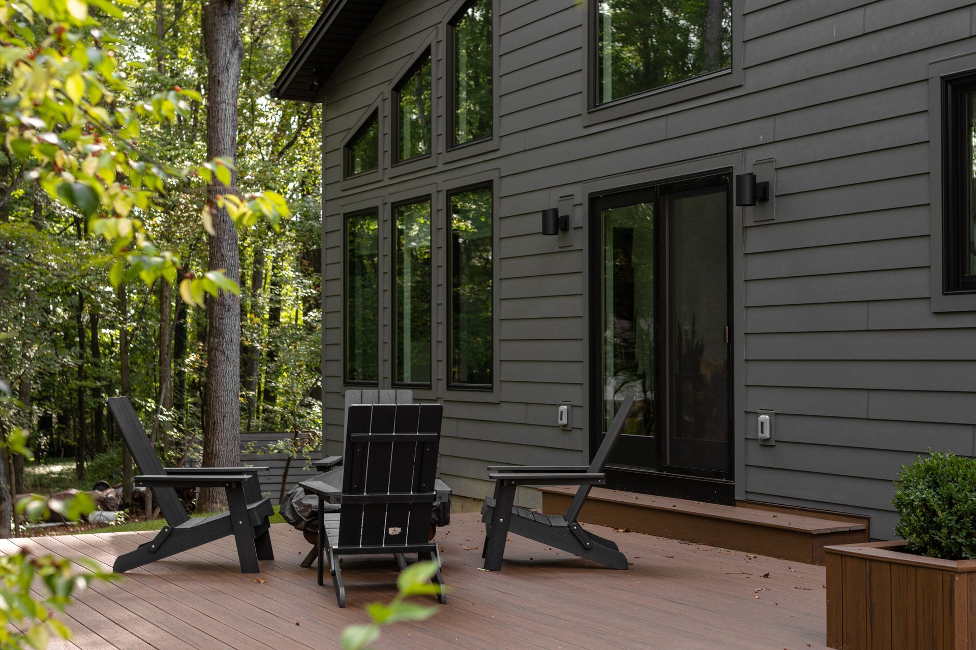 Modern house patio with black chairs, table, and trees beside large windows and sliding door