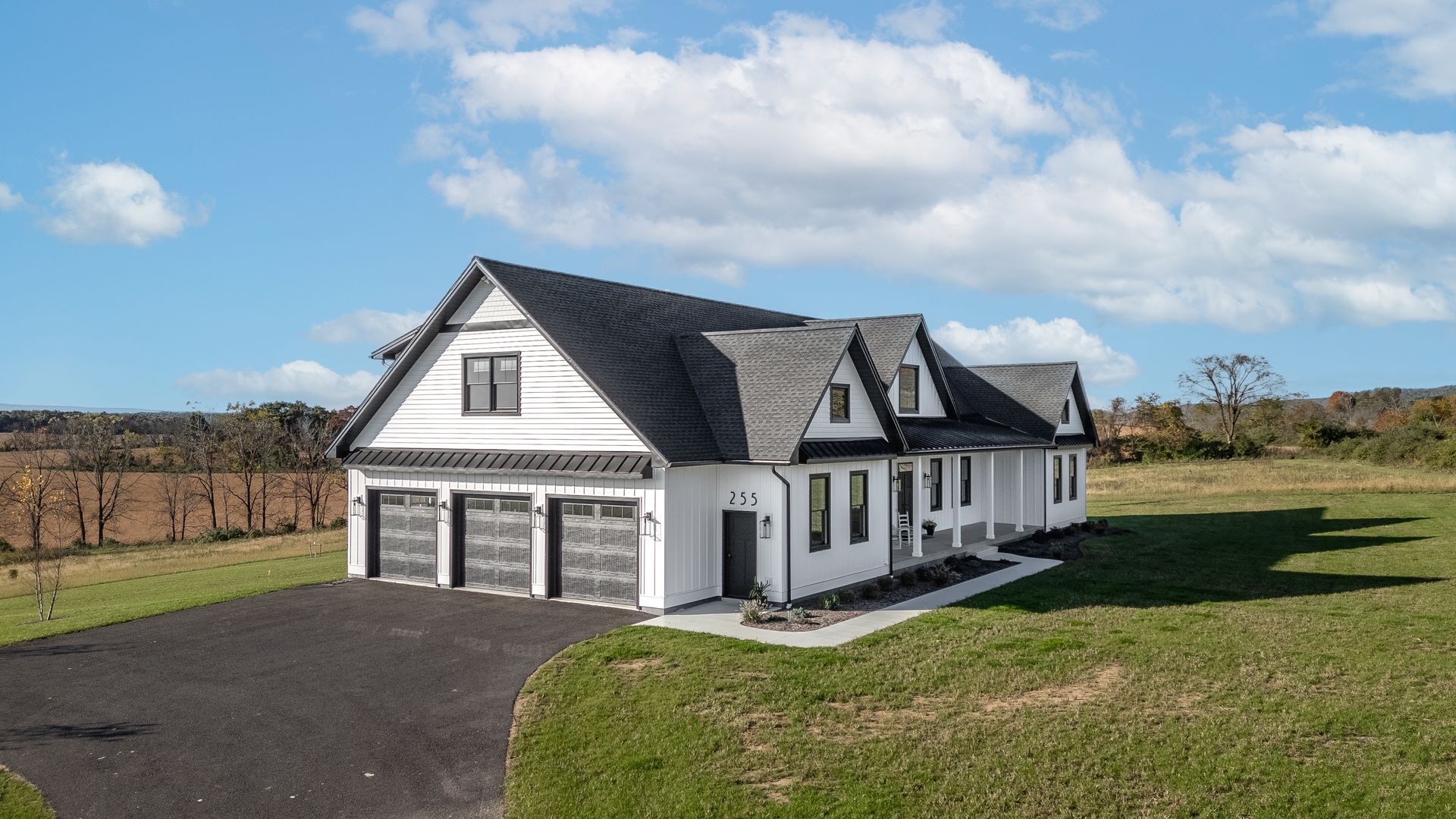 White two-story house with dark roof and garage, on a grassy lot beside a driveway under a blue sky