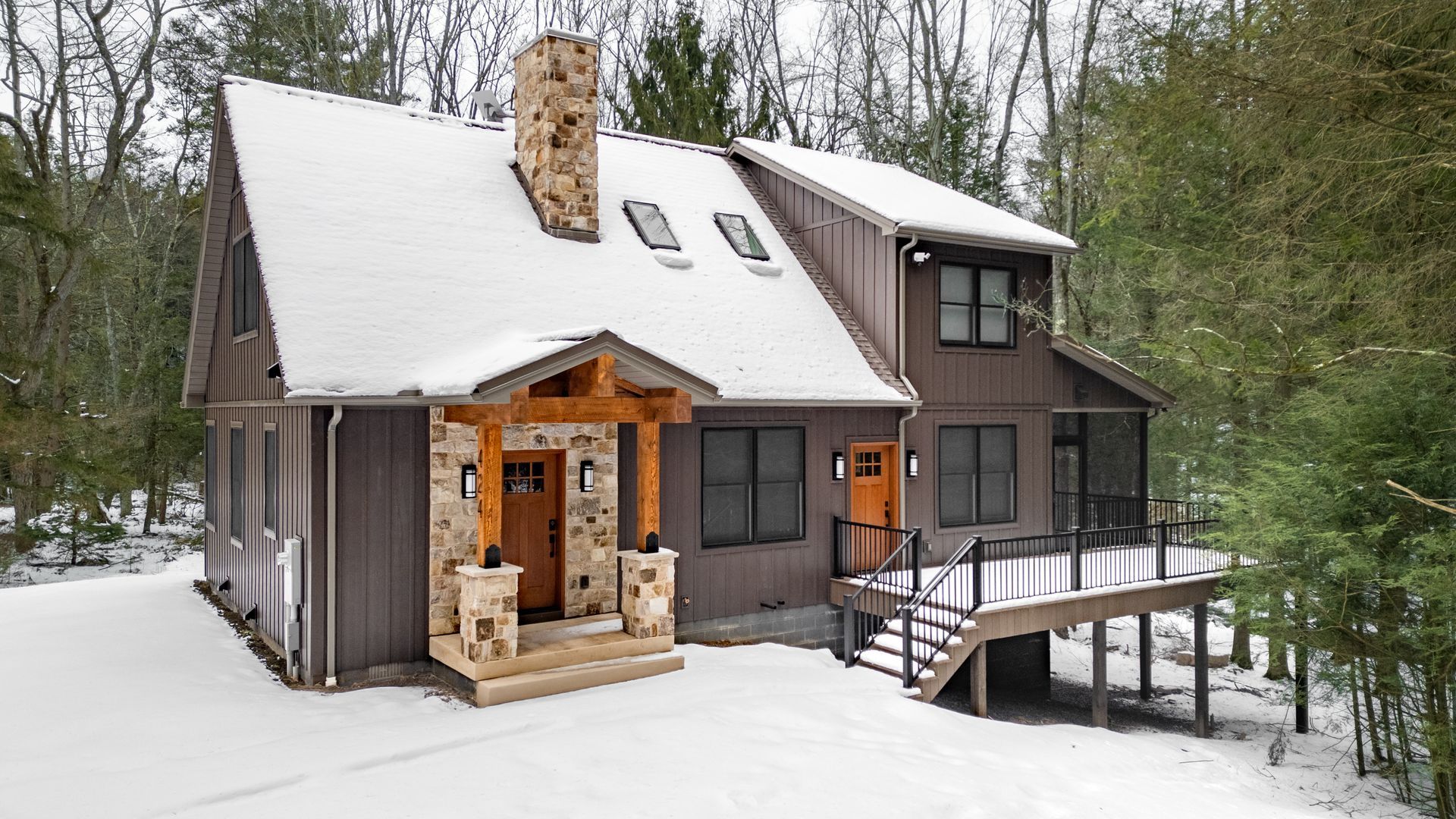 Snow-covered cabin in the woods with a wooden porch and steep roof