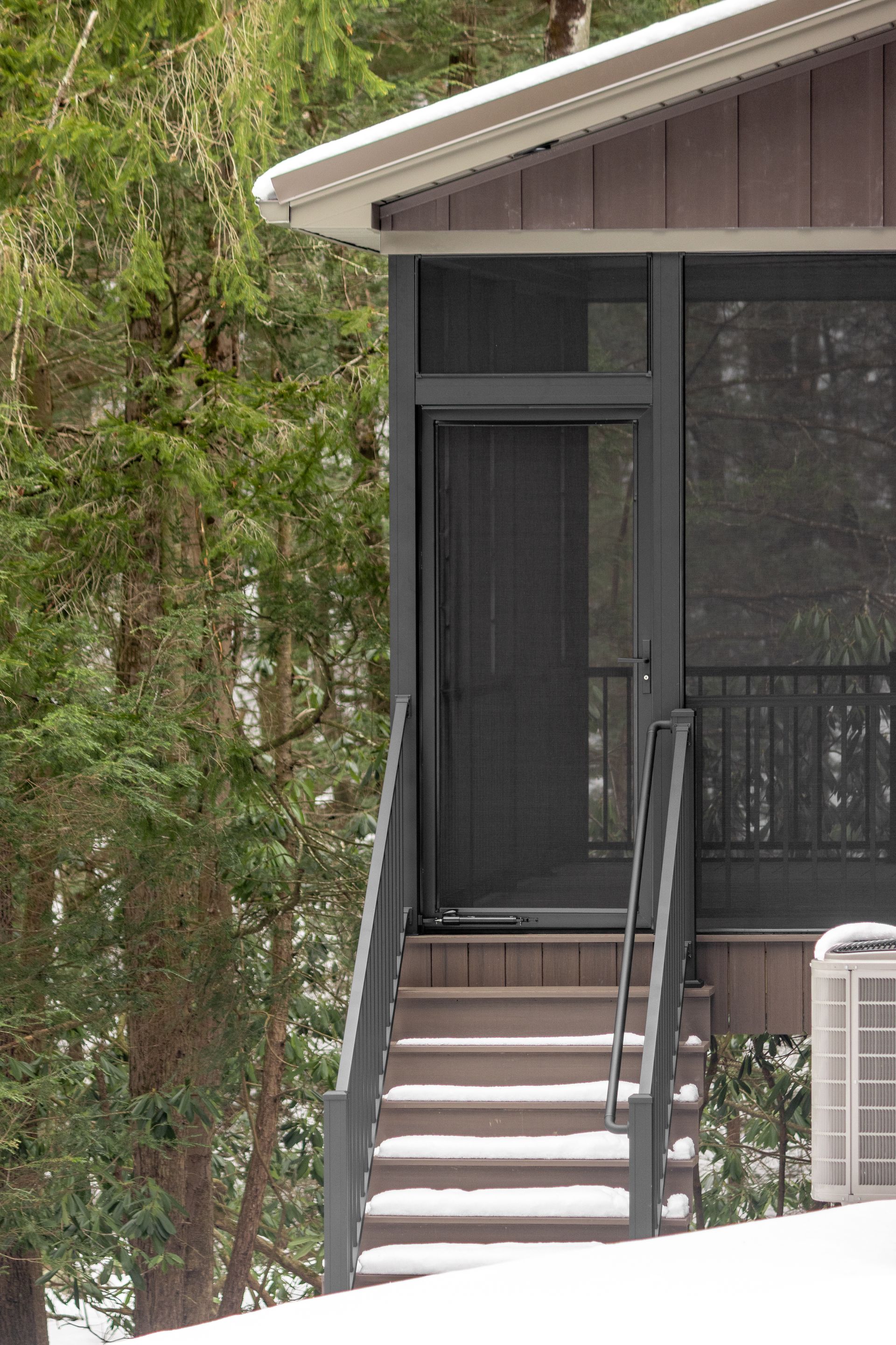 Front entrance of a house with stairs, dark door, and railing beside trees.