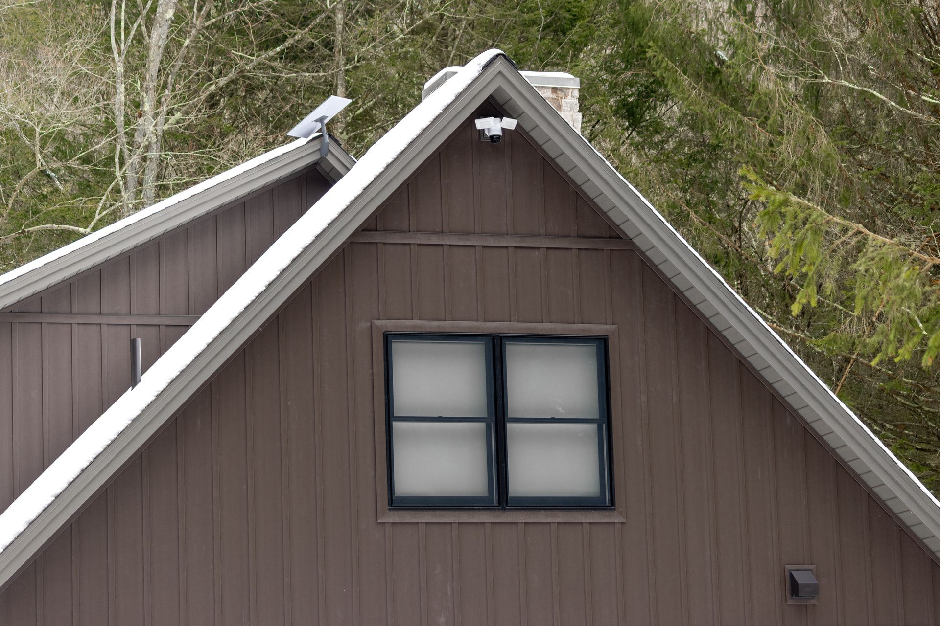 Brown house gable with a blue-framed four-pane window and white trim against trees
