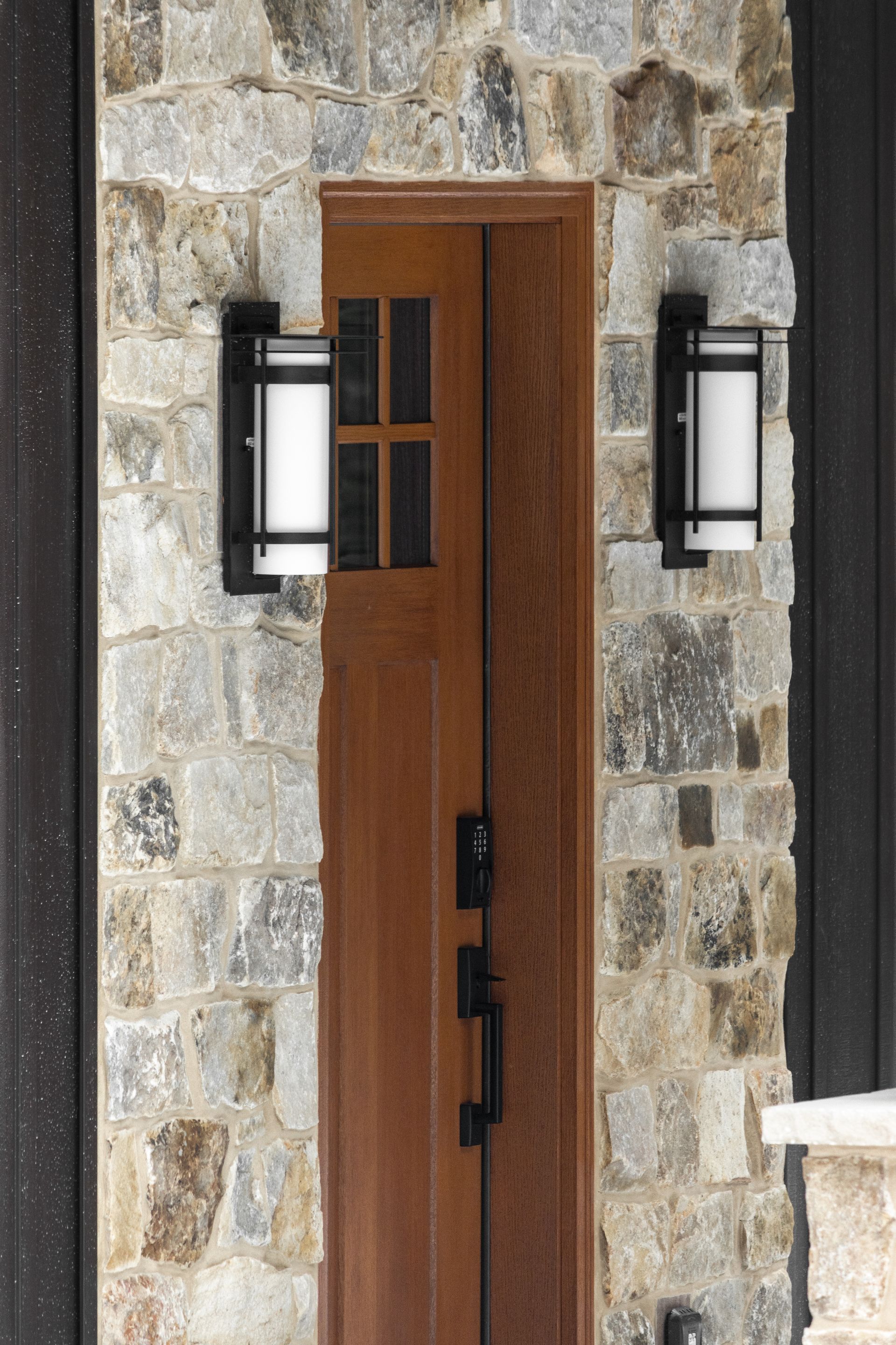 Wooden front door in a stone wall, flanked by two black lantern-style lights.