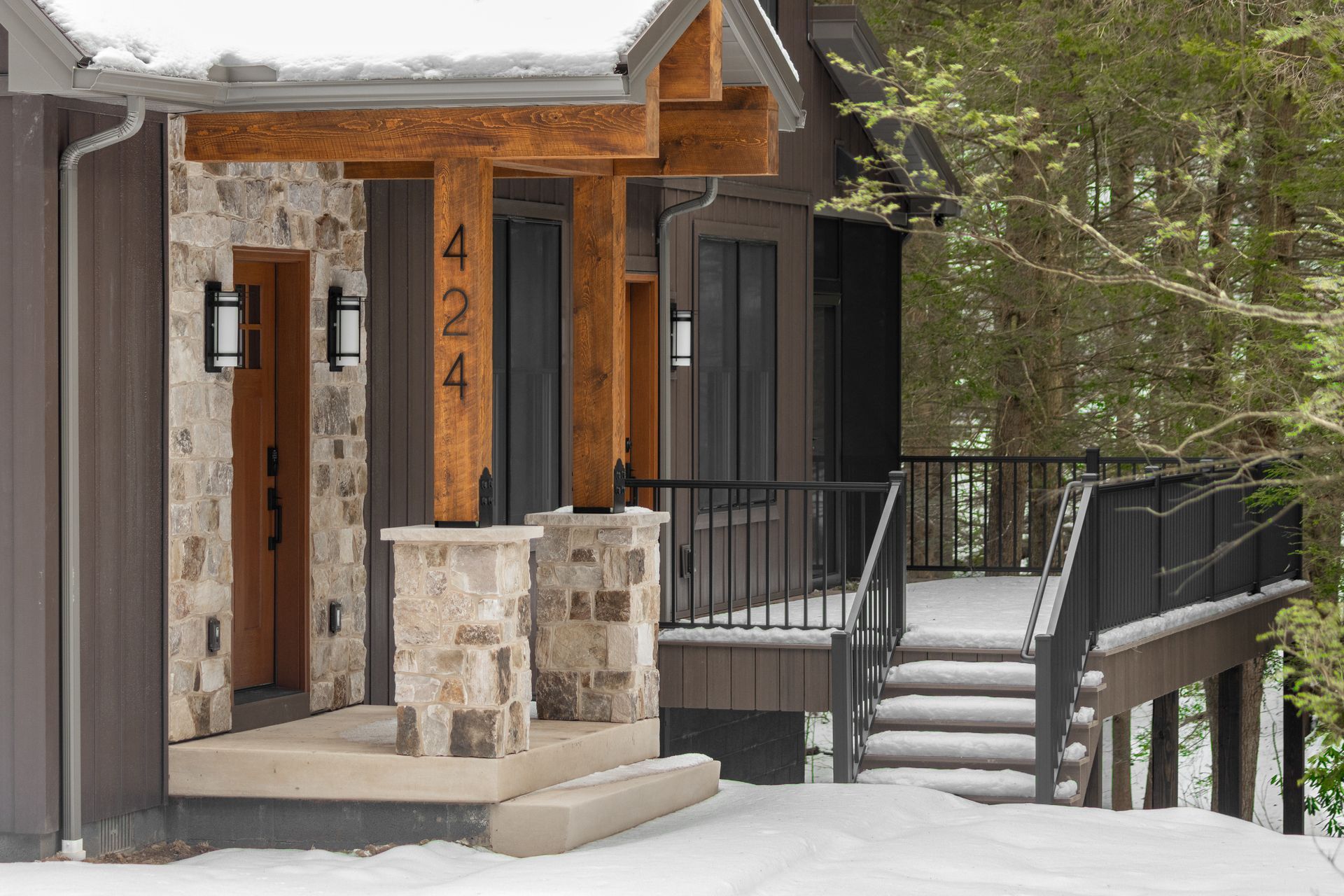 Snowy front porch with stone steps, black railing, and wooden entryway on a house