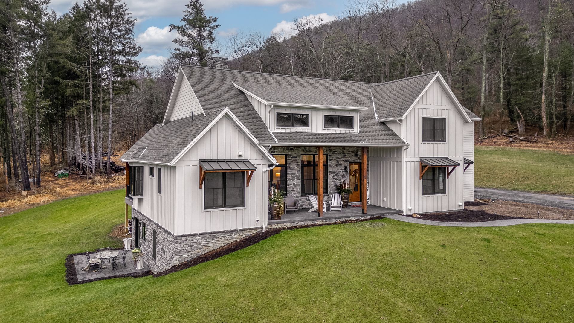 White cottage with dark roof and porch on a green lawn, set against trees and mountains