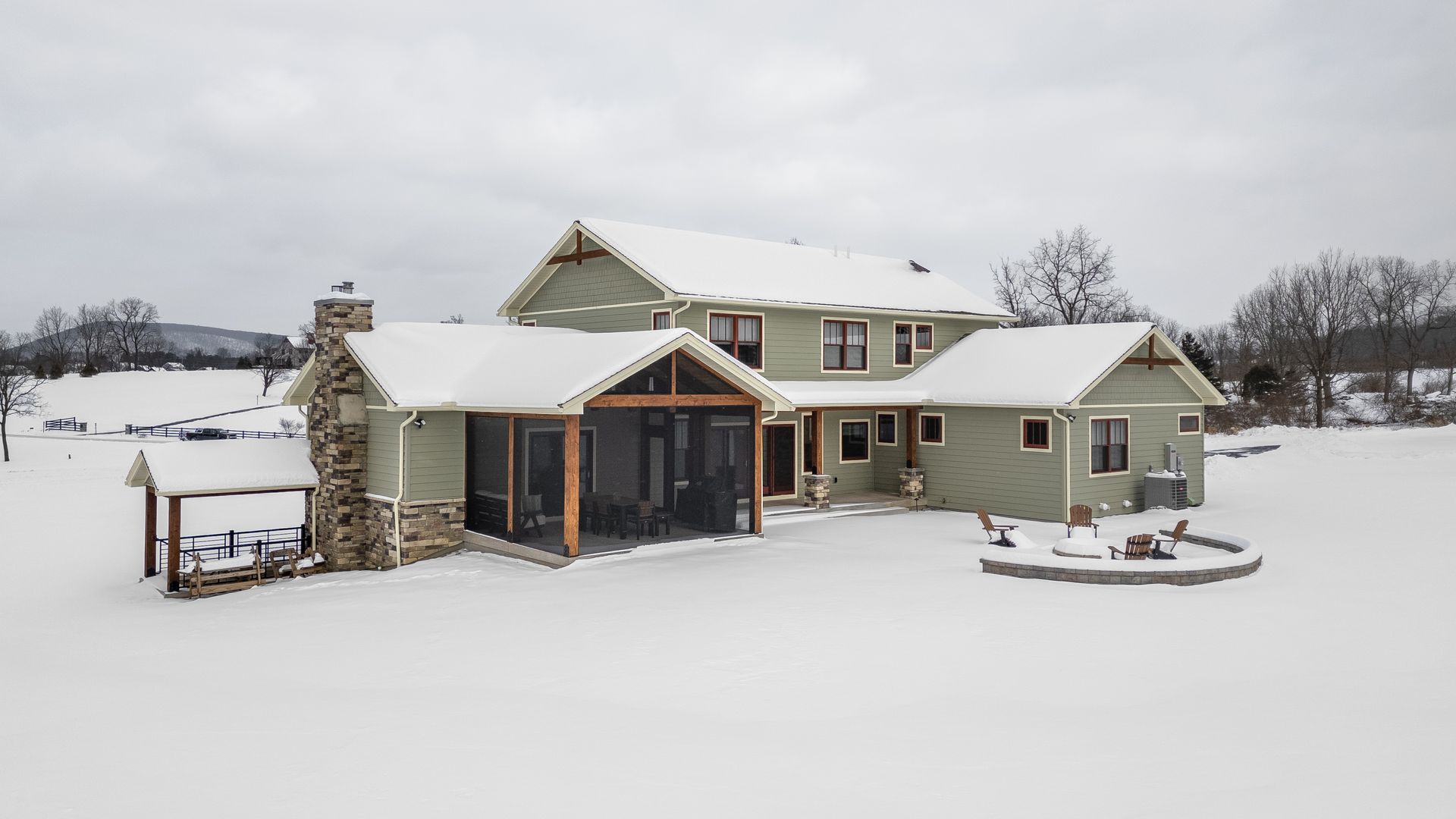 Snow-covered farmhouse with a stone porch, outbuildings, and a snowy yard in winter