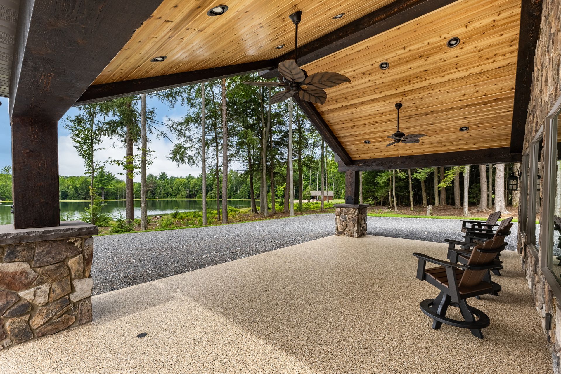 Open-air pavilion with a wood ceiling, stone columns, and chairs overlooking a landscaped garden
