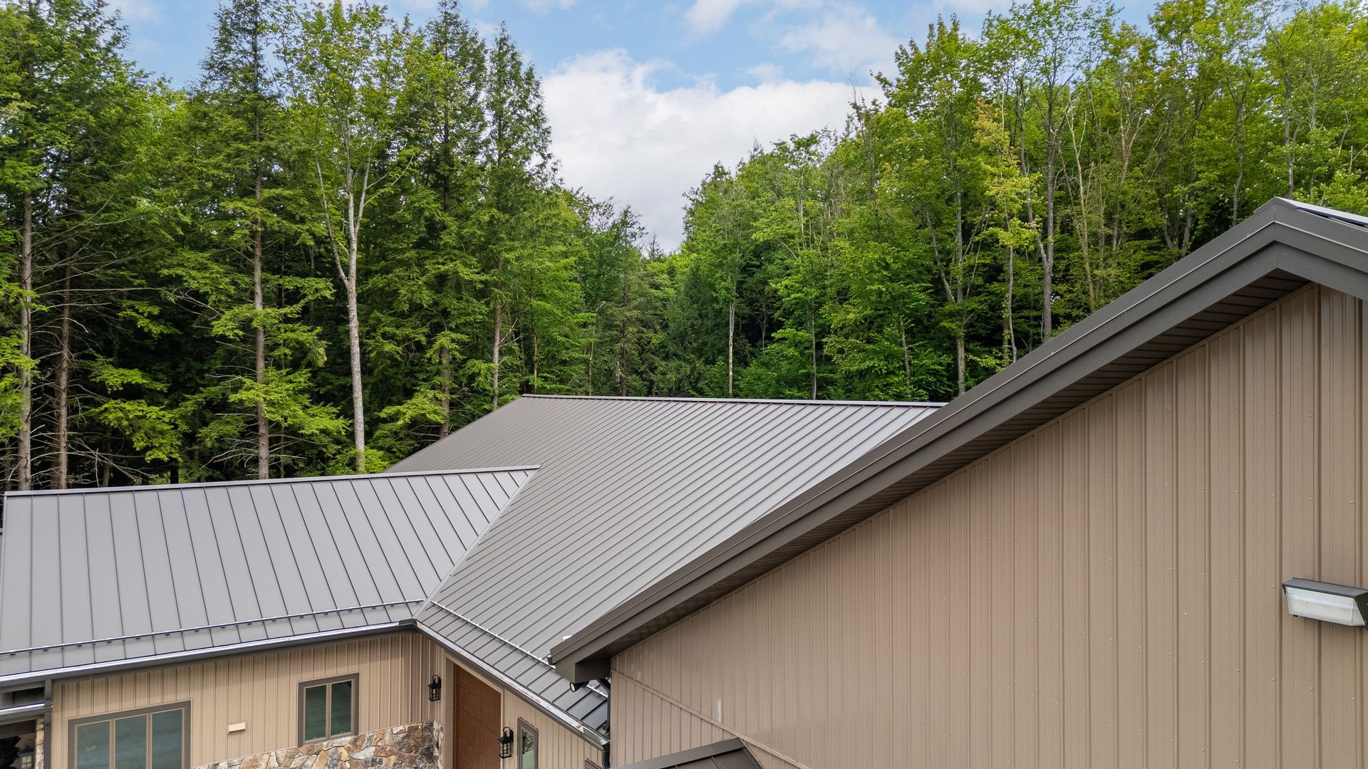 Cabin rooftops with tan siding in a forested hillside setting under a partly cloudy sky
