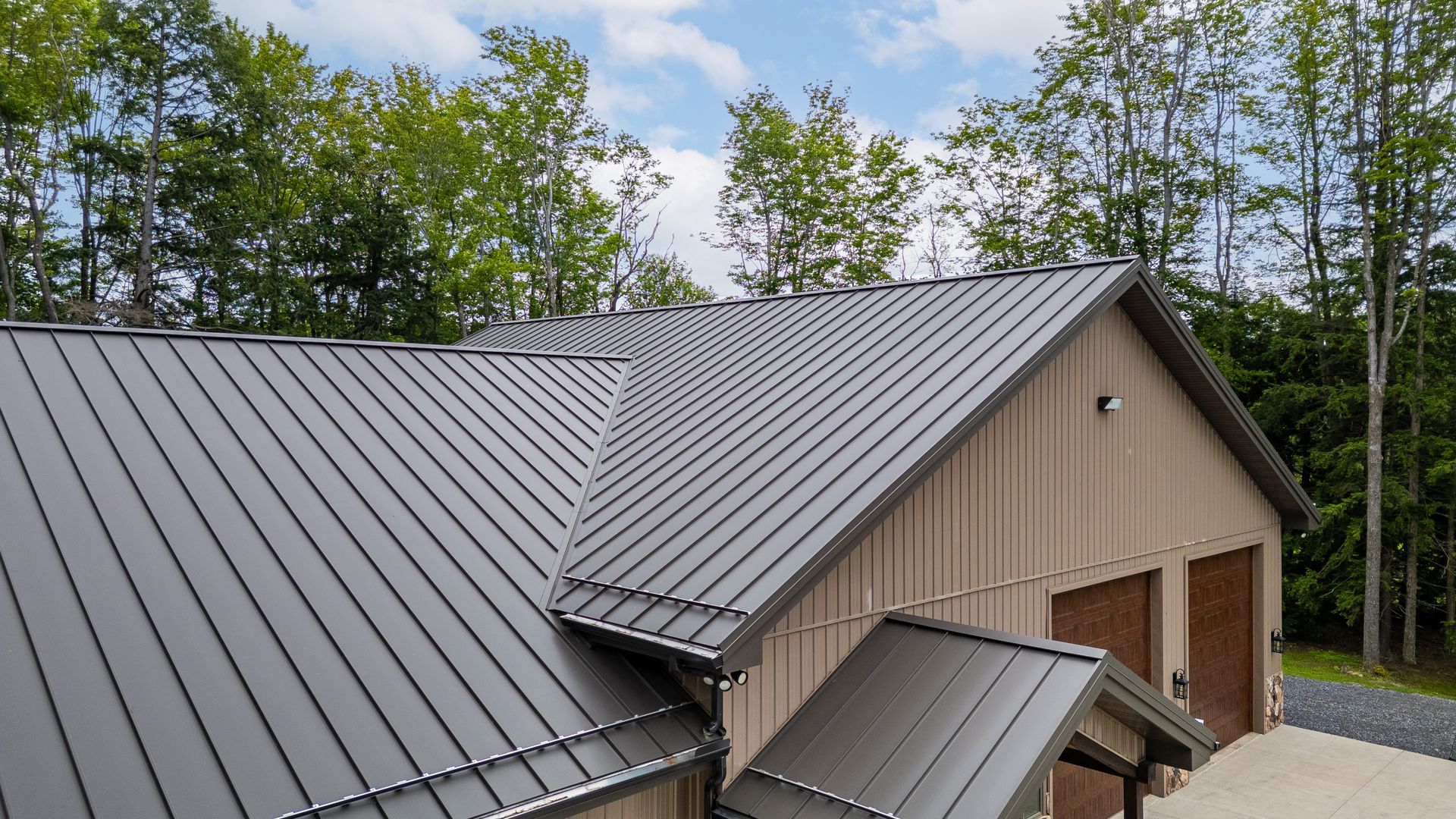 Metal-roofed house with dormers and wooden doors, surrounded by trees under a cloudy sky