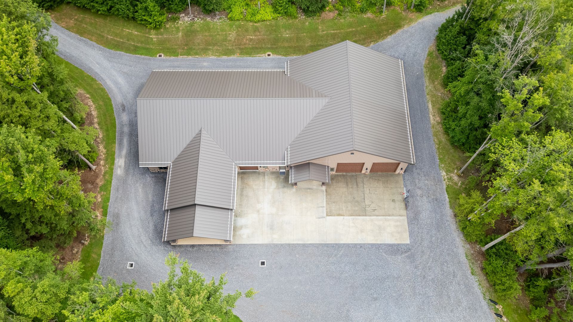 Aerial view of a house with a gray roof, driveway, and surrounding trees.