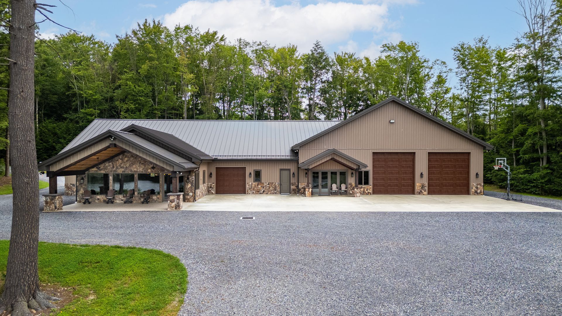 Modern single-story house with covered porch, two garage doors, and a gravel driveway surrounded by trees
