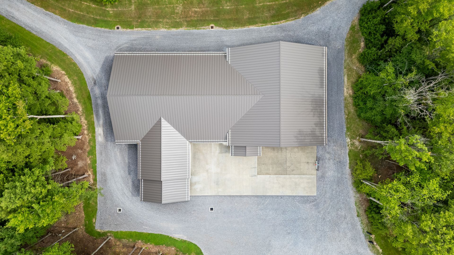 Top-down view of a house with a gray roof, gravel driveway, and surrounding green landscaping.
