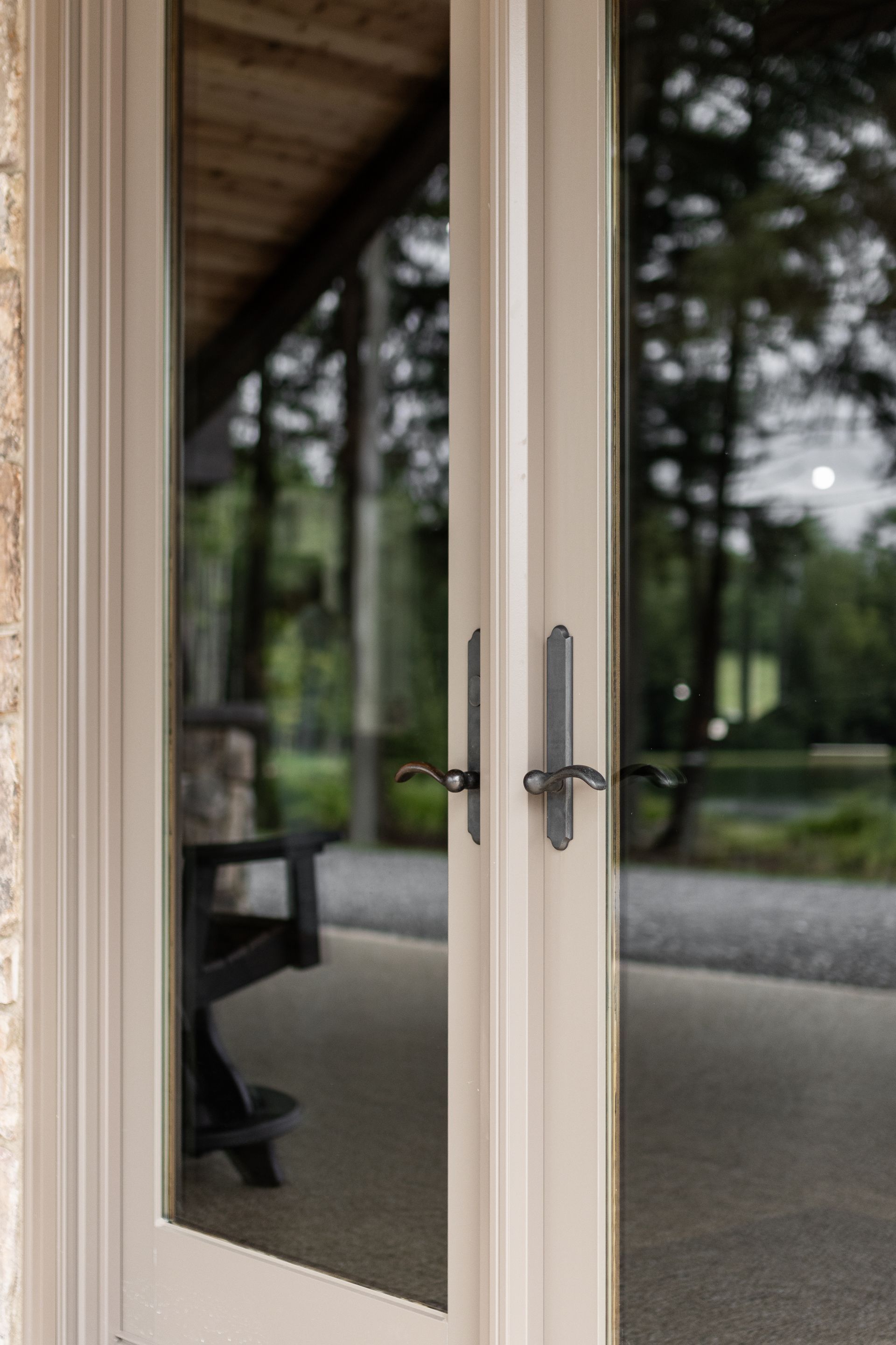 Glass patio doors with beige frames reflecting a tree-lined outdoor walkway