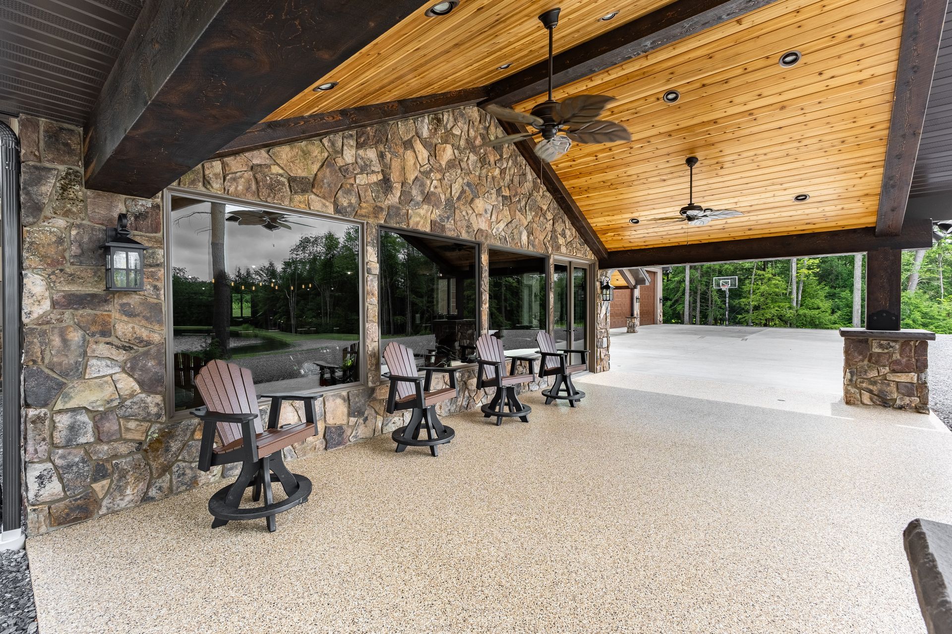 Covered stone patio with several rocking chairs and tables beneath a wood ceiling