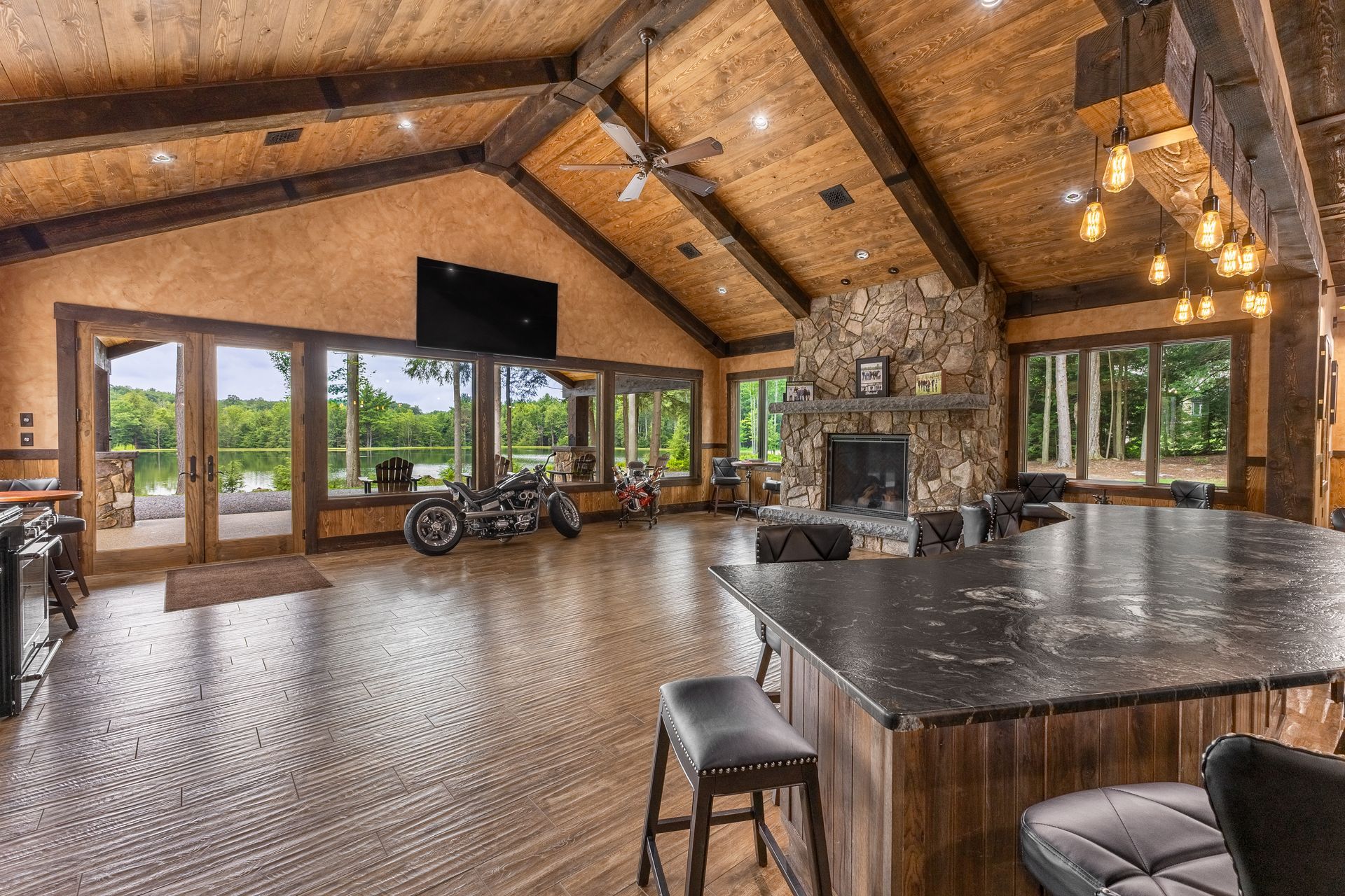 Spacious rustic lodge interior with vaulted wood ceiling, stone fireplace, large windows, and a billiard table