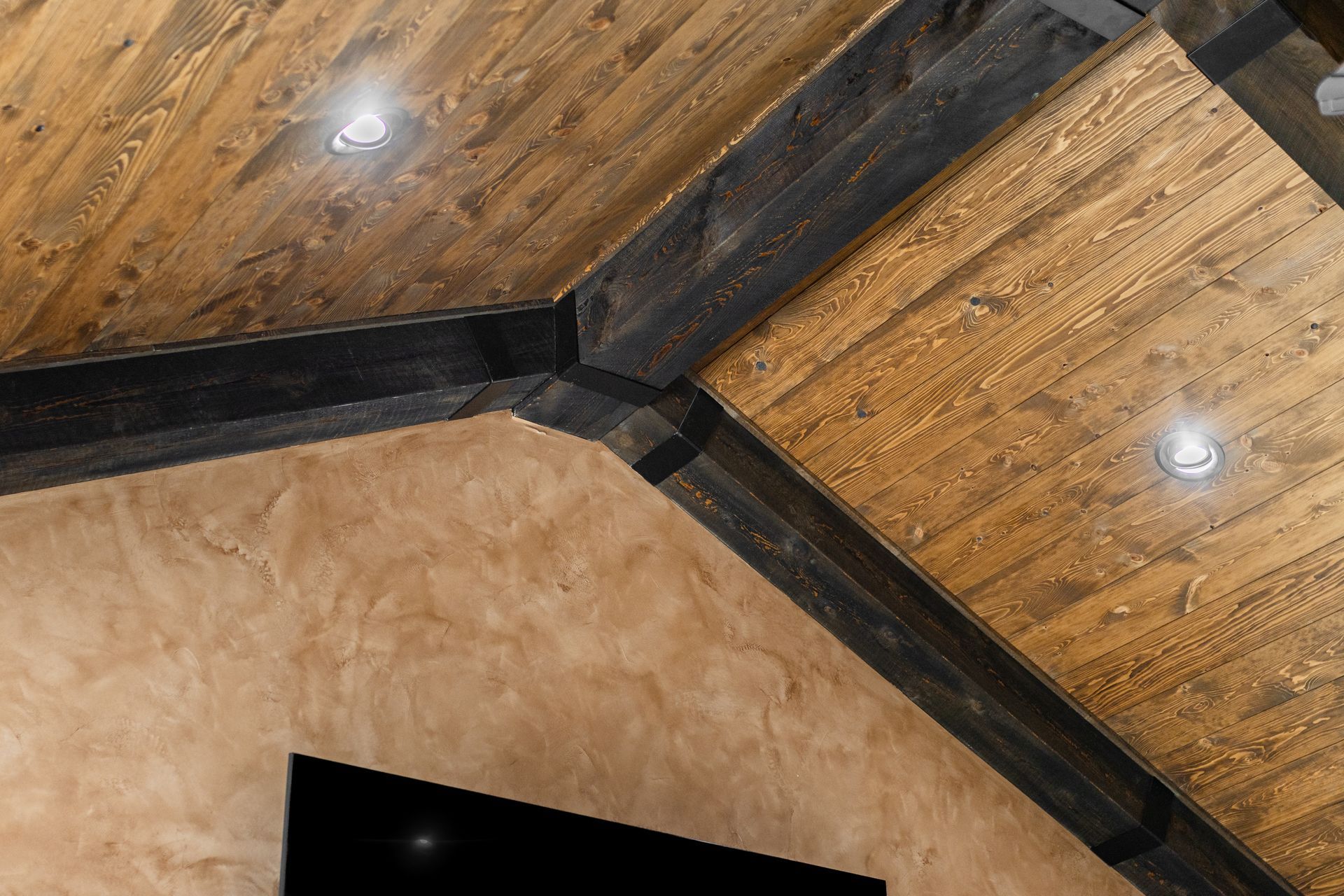 Wooden ceiling with dark beams and recessed lights above a beige stucco wall