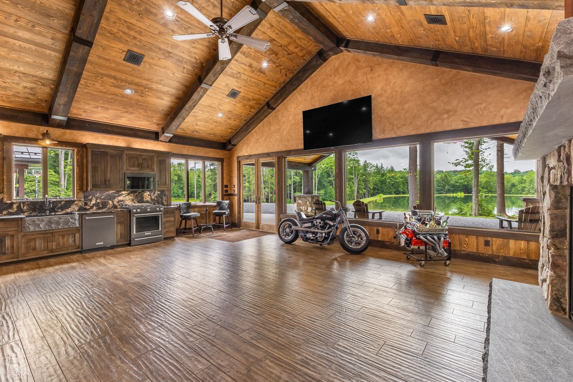 Spacious rustic lodge living room with wood beams, stone fireplace, large windows, and mountain views
