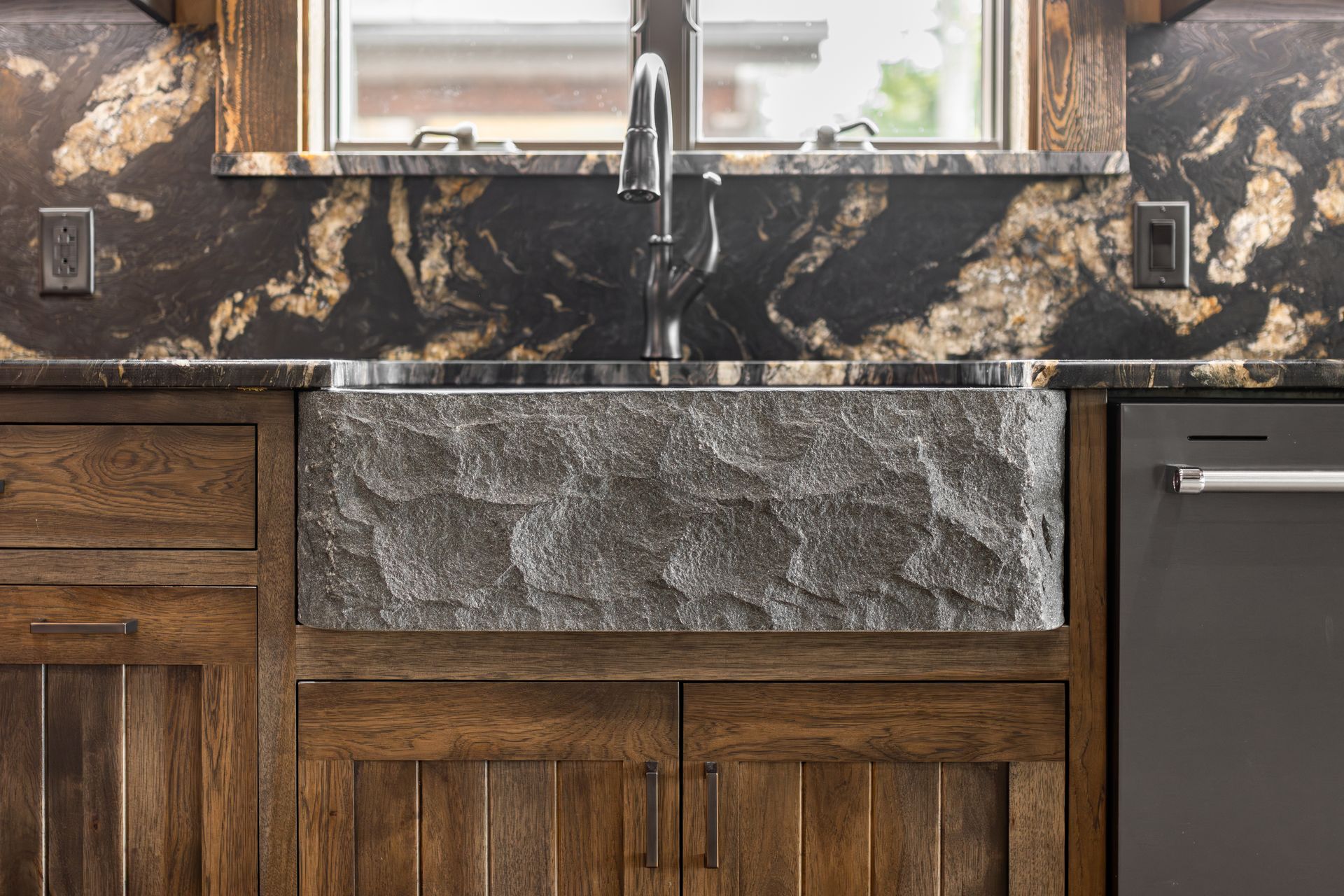 Rustic kitchen sink with dark granite countertop, farmhouse basin, and black faucet beneath a window