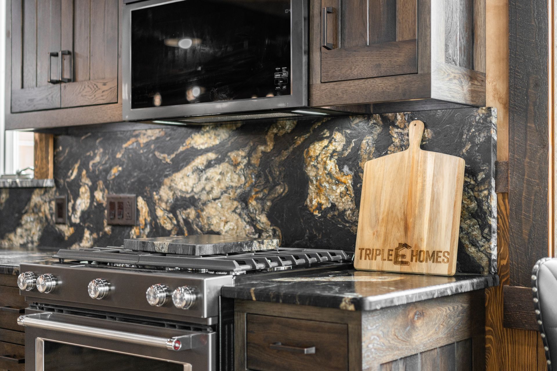 Modern kitchen with dark cabinets, gas stove, black marble backsplash, and wooden cutting board on the counter