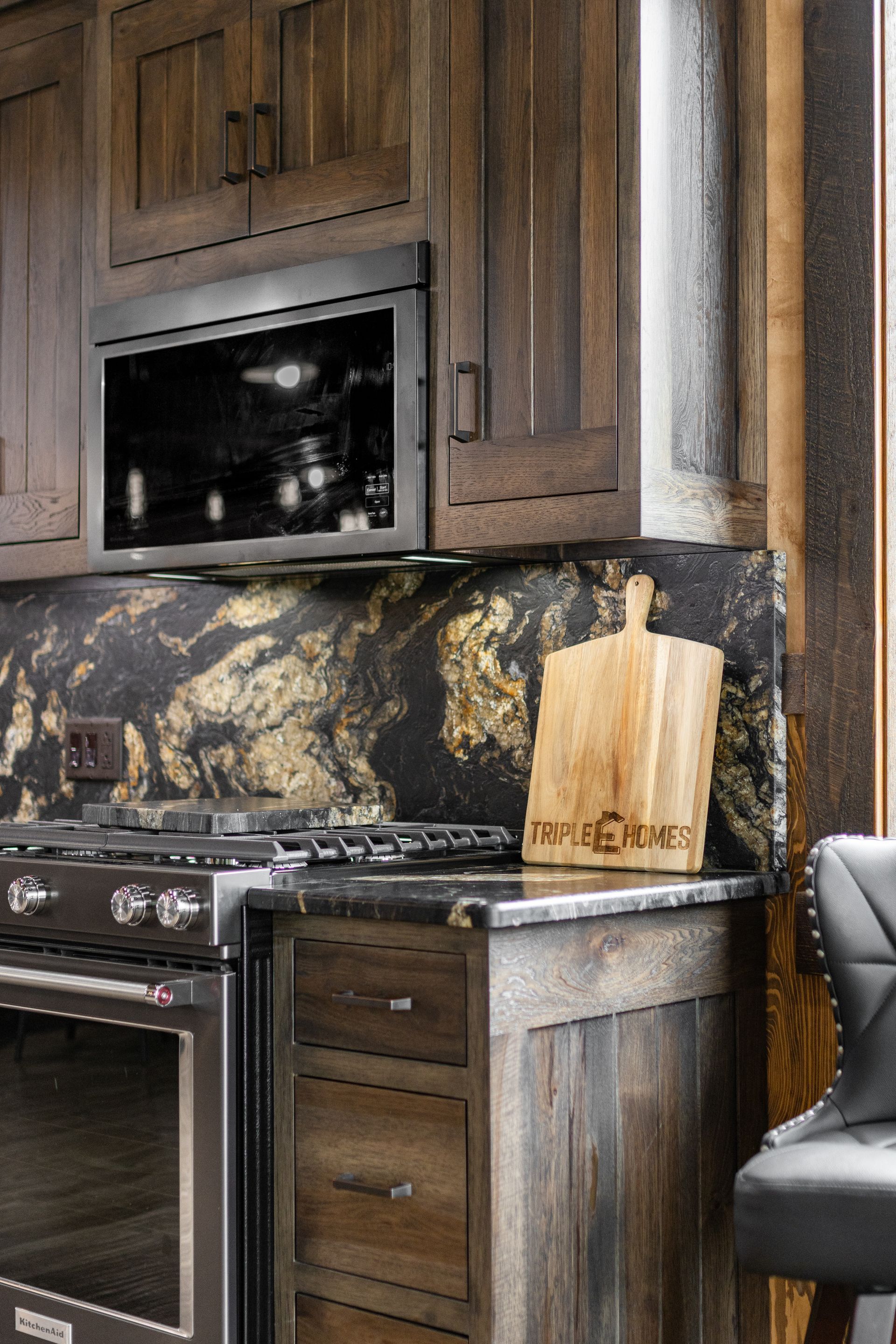 Modern kitchen with dark wood cabinets, black marble backsplash, oven, and a cutting board on the counter