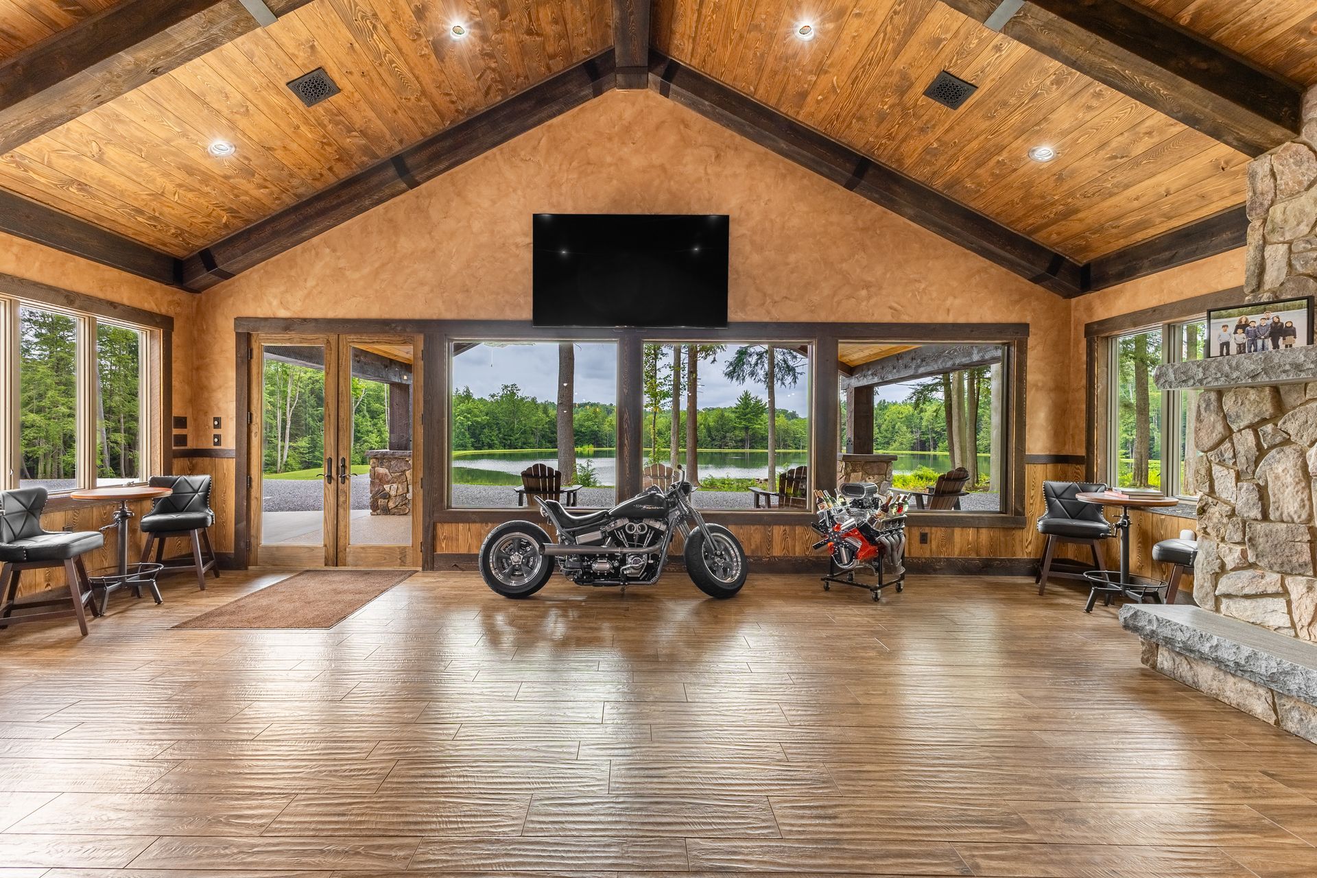 Lodge interior with glass walls, wood beams, fireplace, and two motorcycles centered on a polished floor.