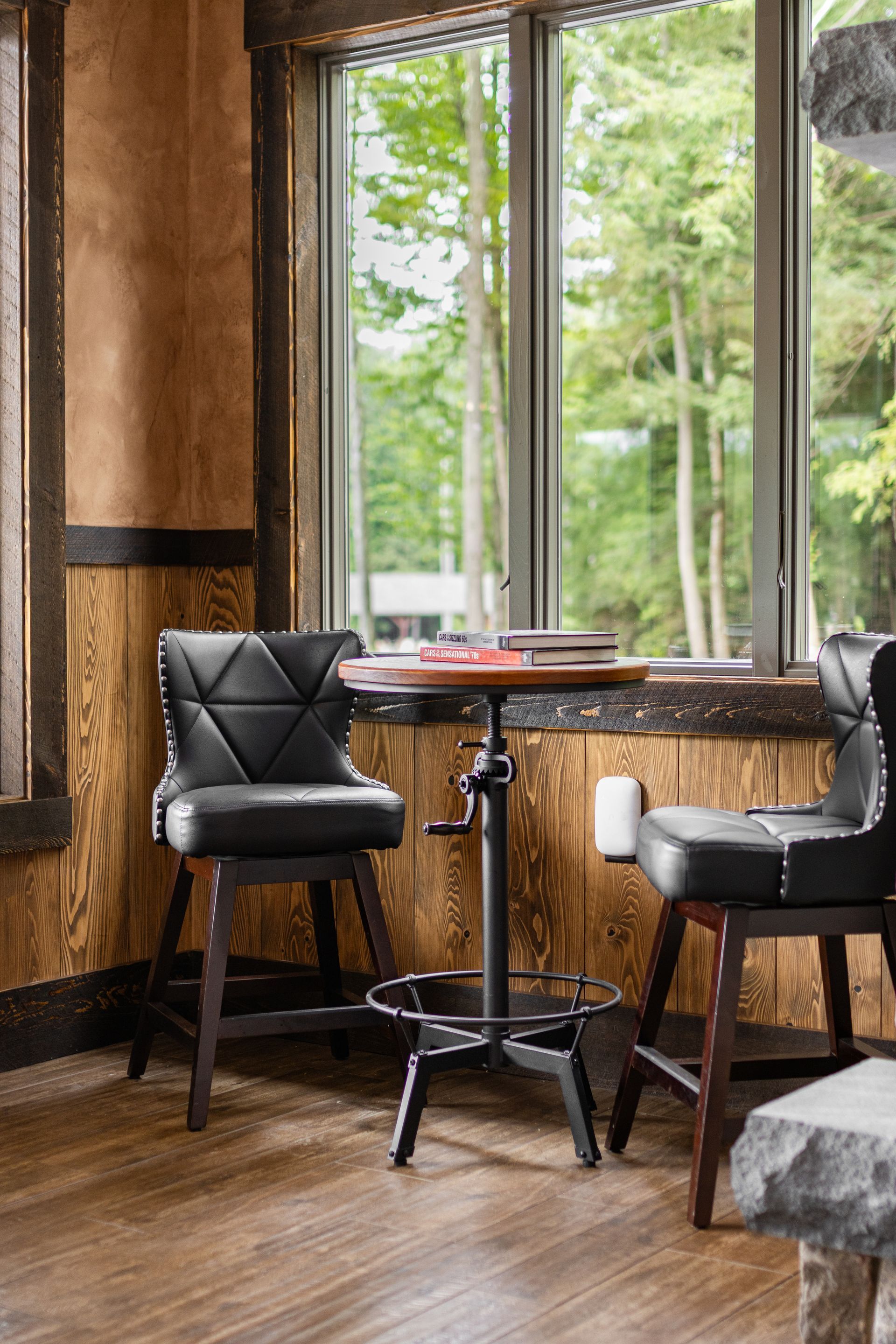Cozy café corner with two black chairs, a small table, and large windows overlooking trees