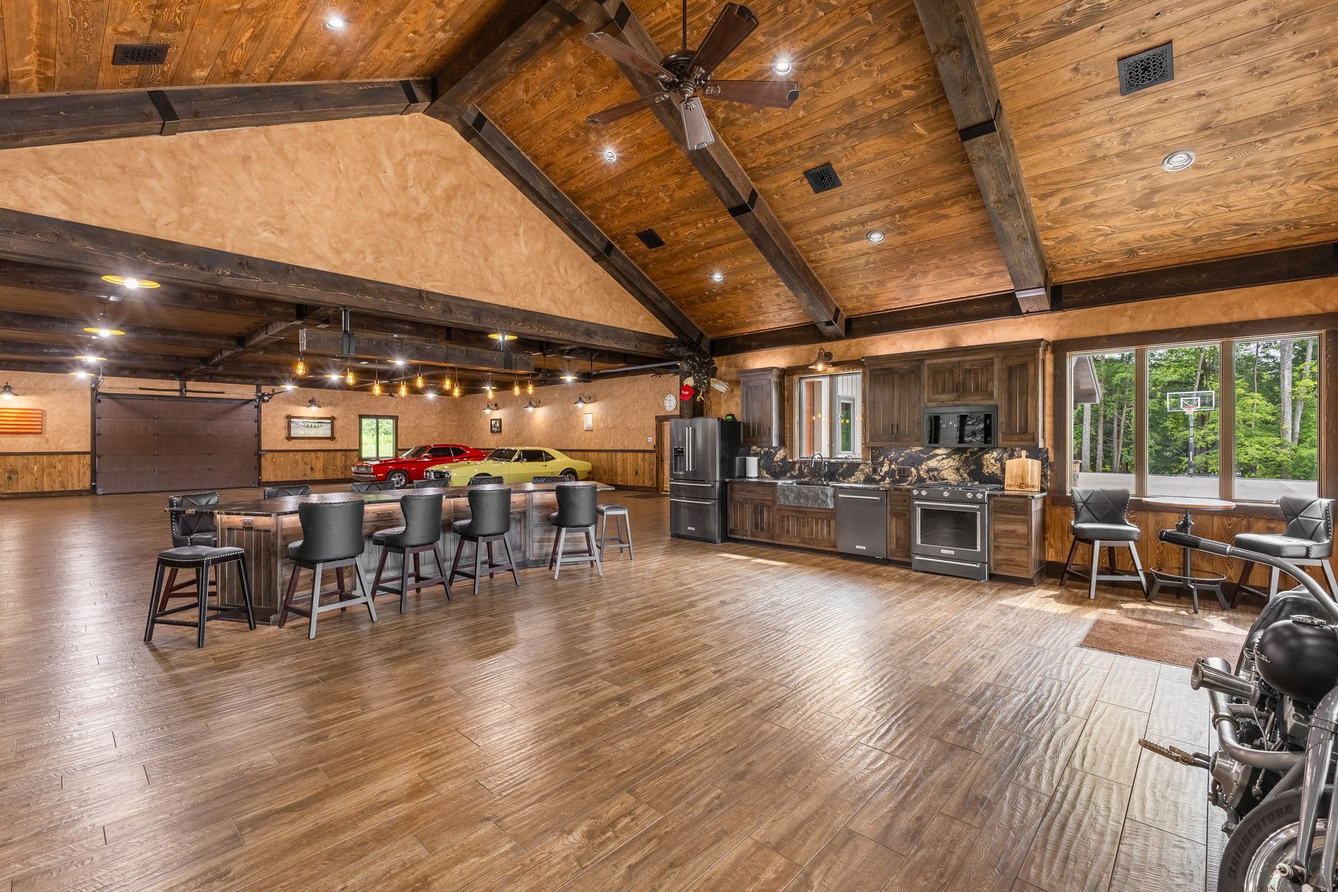 Spacious rustic bar and lounge with wood ceiling, pool tables, stools, and large windows overlooking greenery
