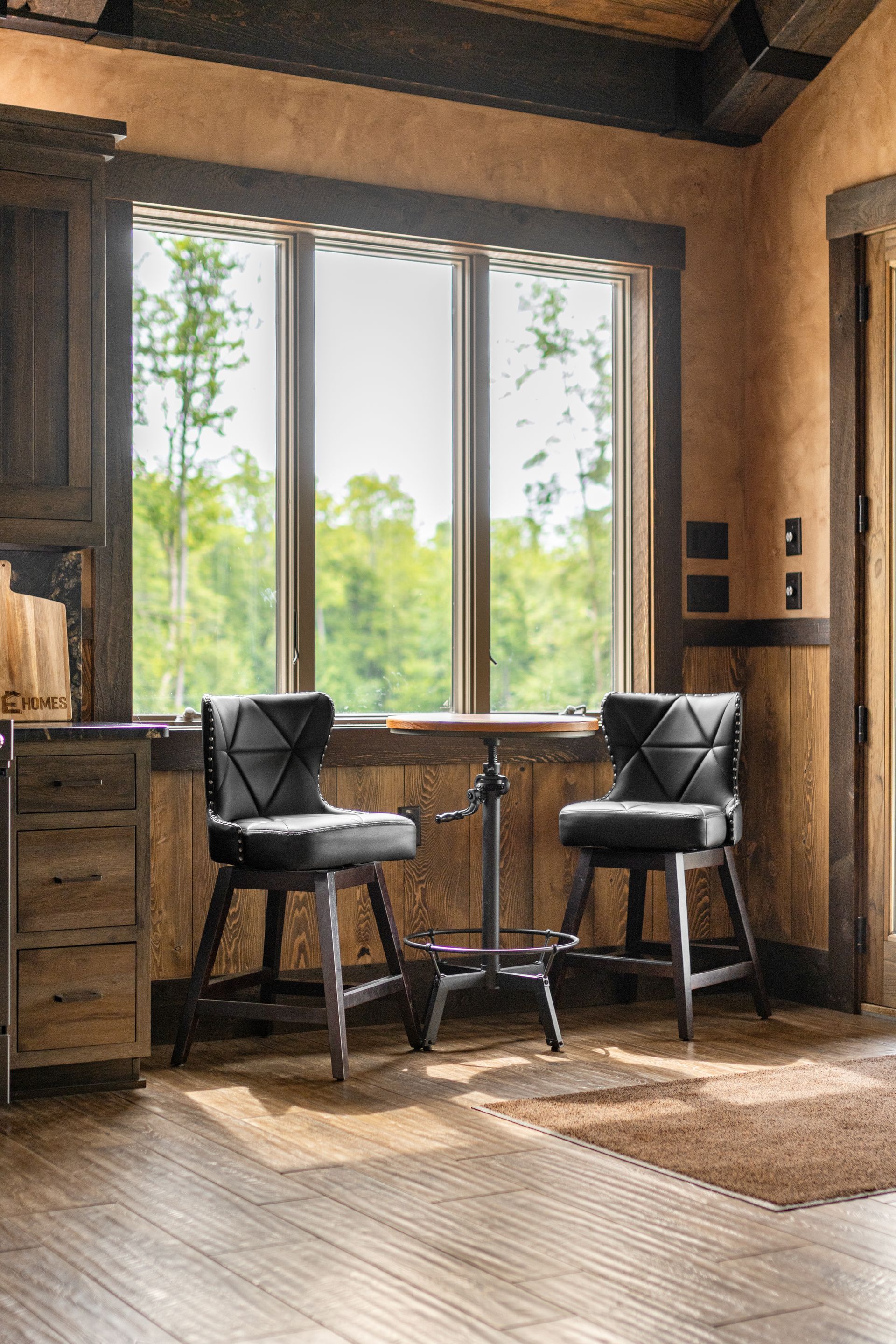 Cozy sunlit room with two black chairs by a large window and wooden furniture