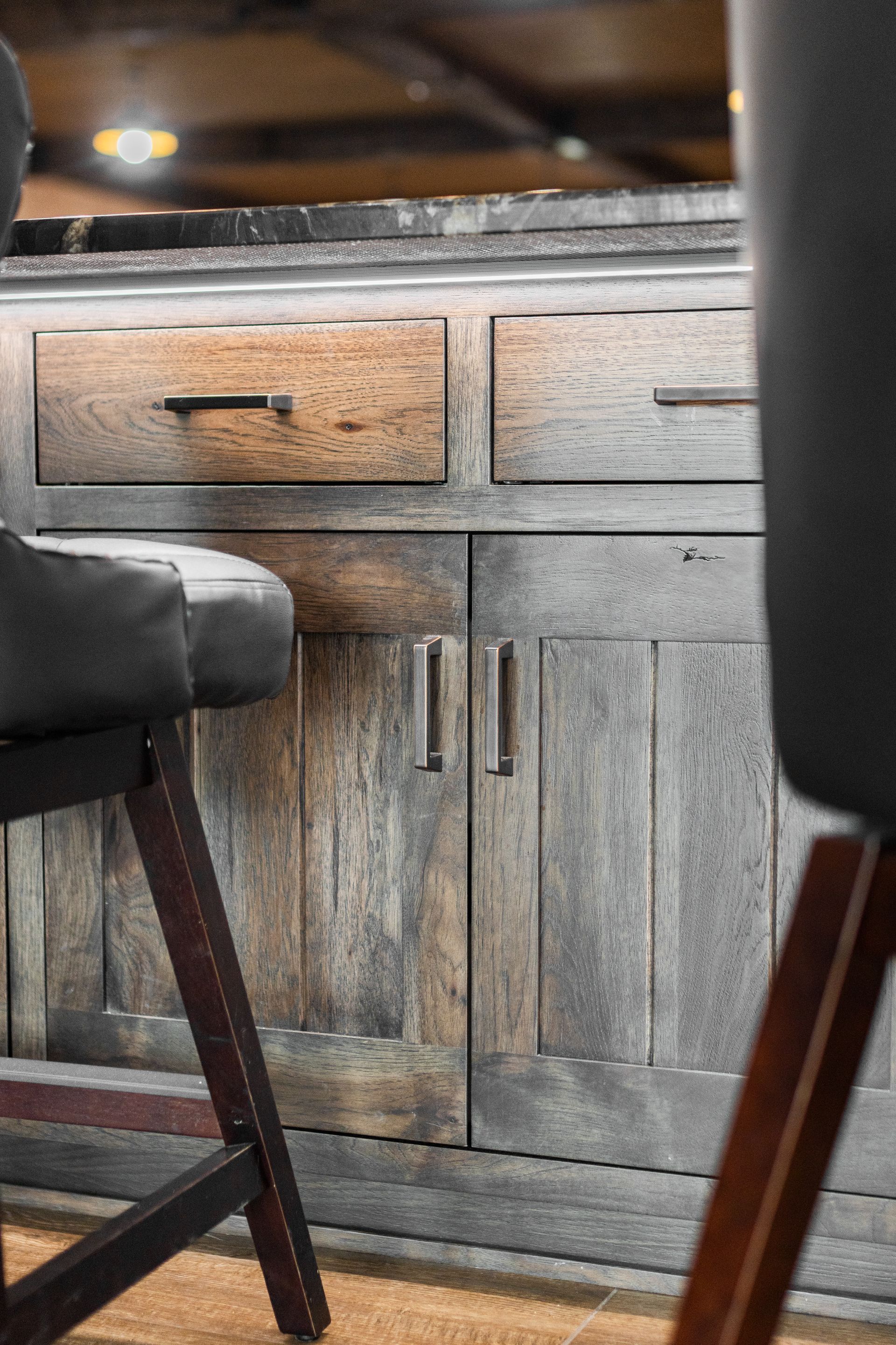 Rustic kitchen cabinets beneath a counter, with two dark stools in the foreground.