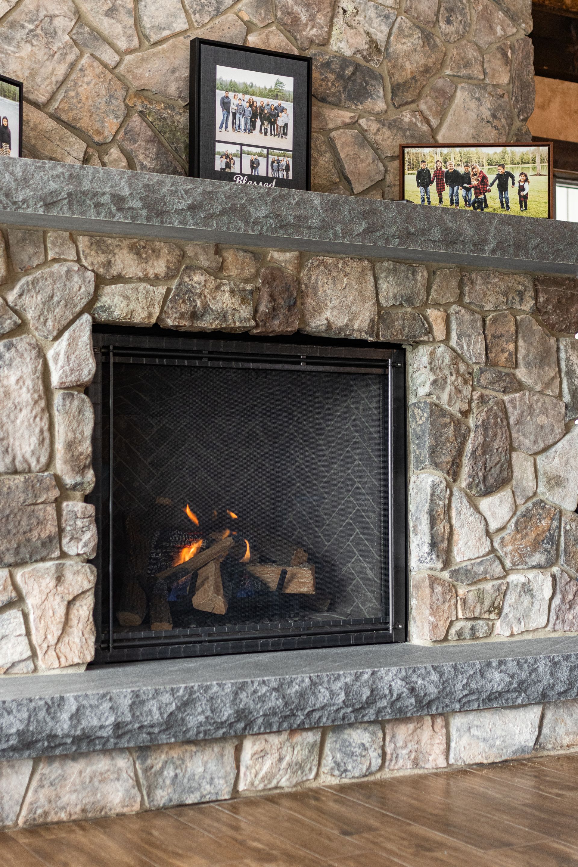 Stone fireplace with a dark mantel, framed photos, and a small fire burning behind a screen.