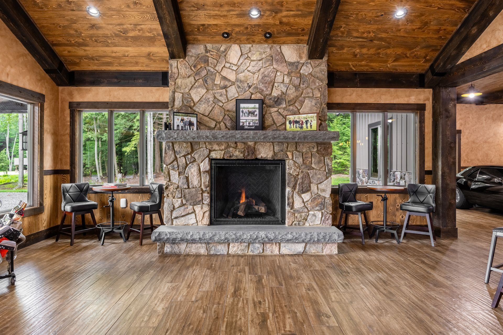 Rustic living room with stone fireplace, wood beams, large windows, and leather chairs