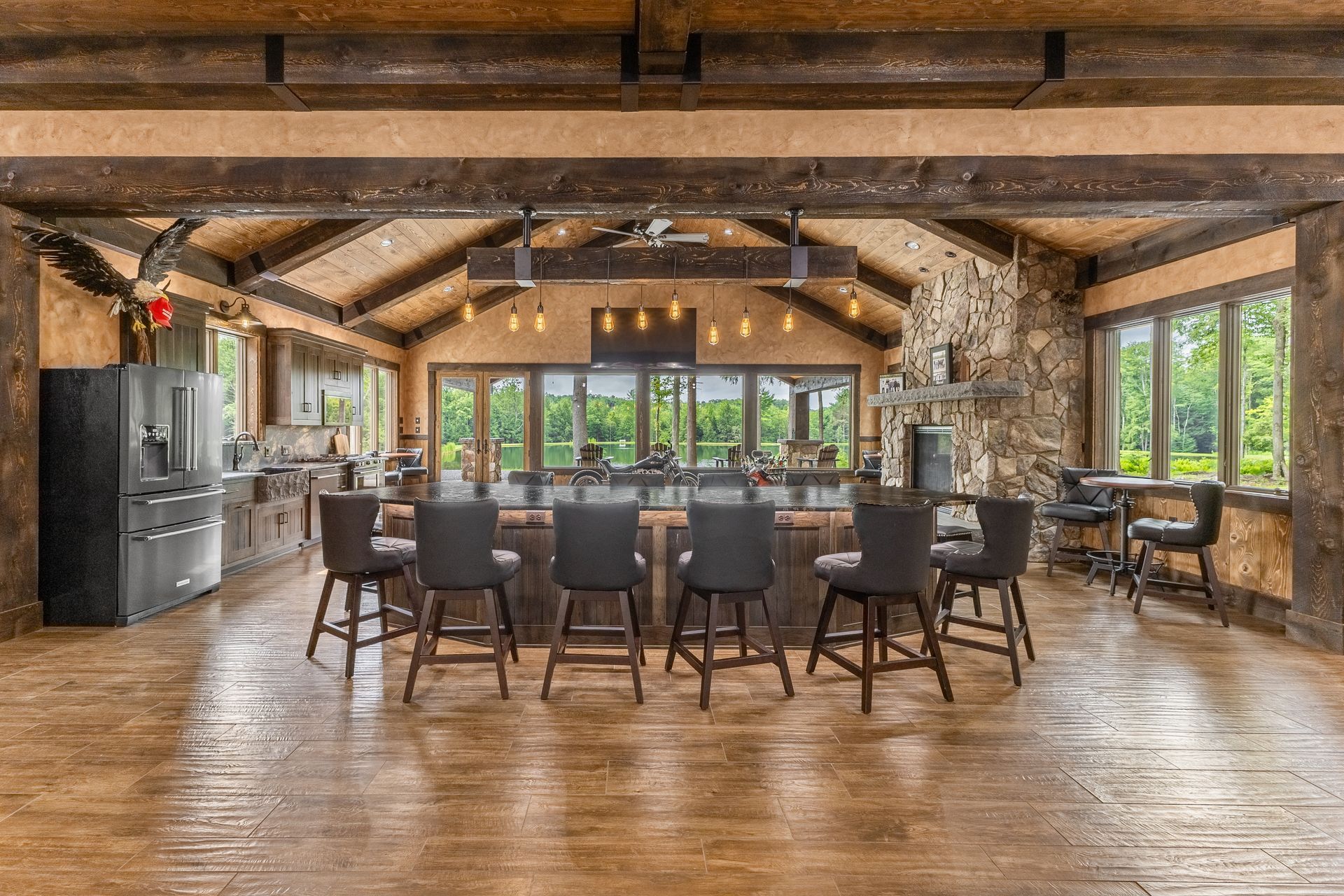 Rustic lodge dining room with long wooden table, dark chairs, stone fireplace, and large windows