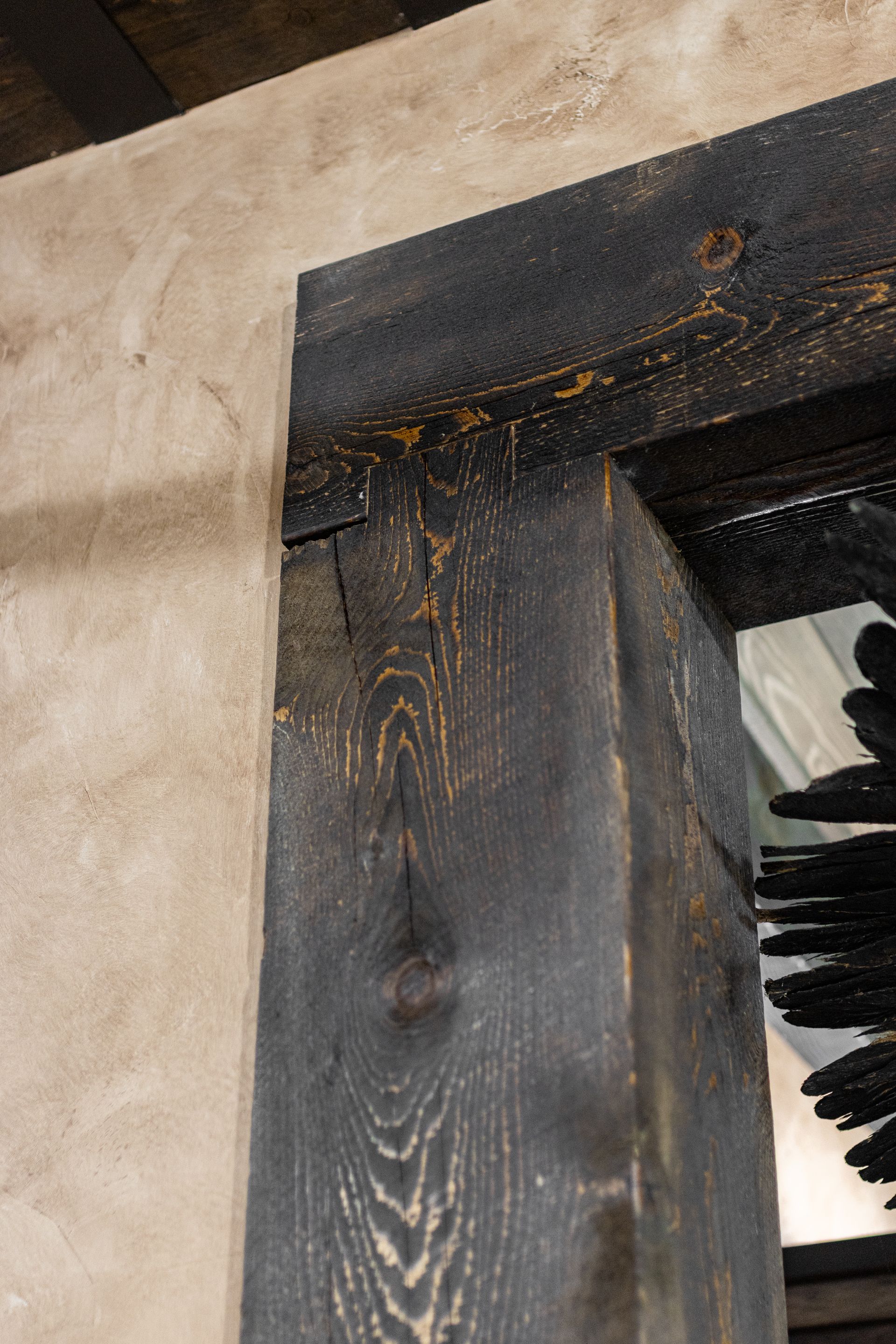 Close-up of a charred black wooden beam against a beige wall with rust-colored stains.