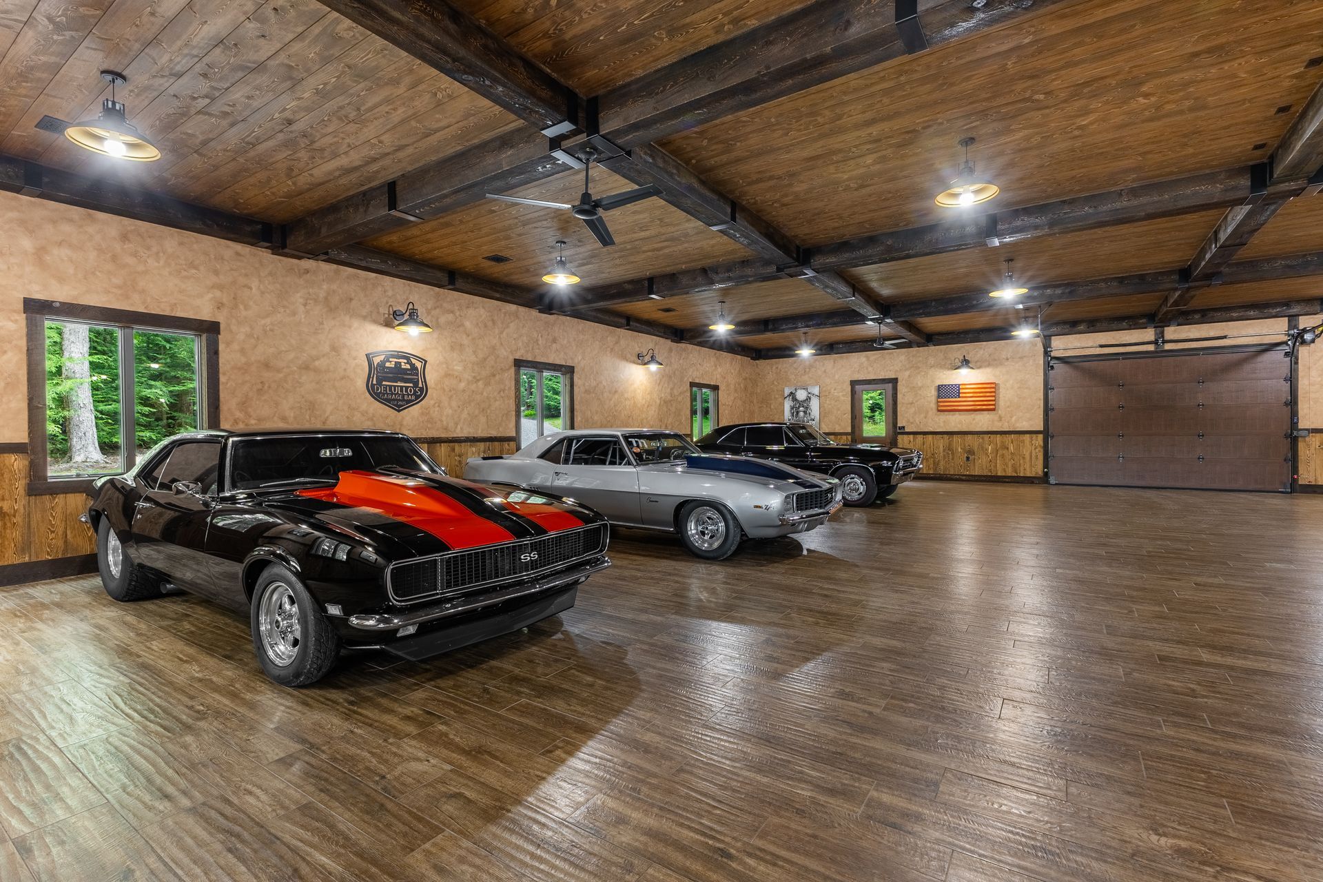 Spacious garage showroom with three sports cars on a polished floor and exposed wood ceiling