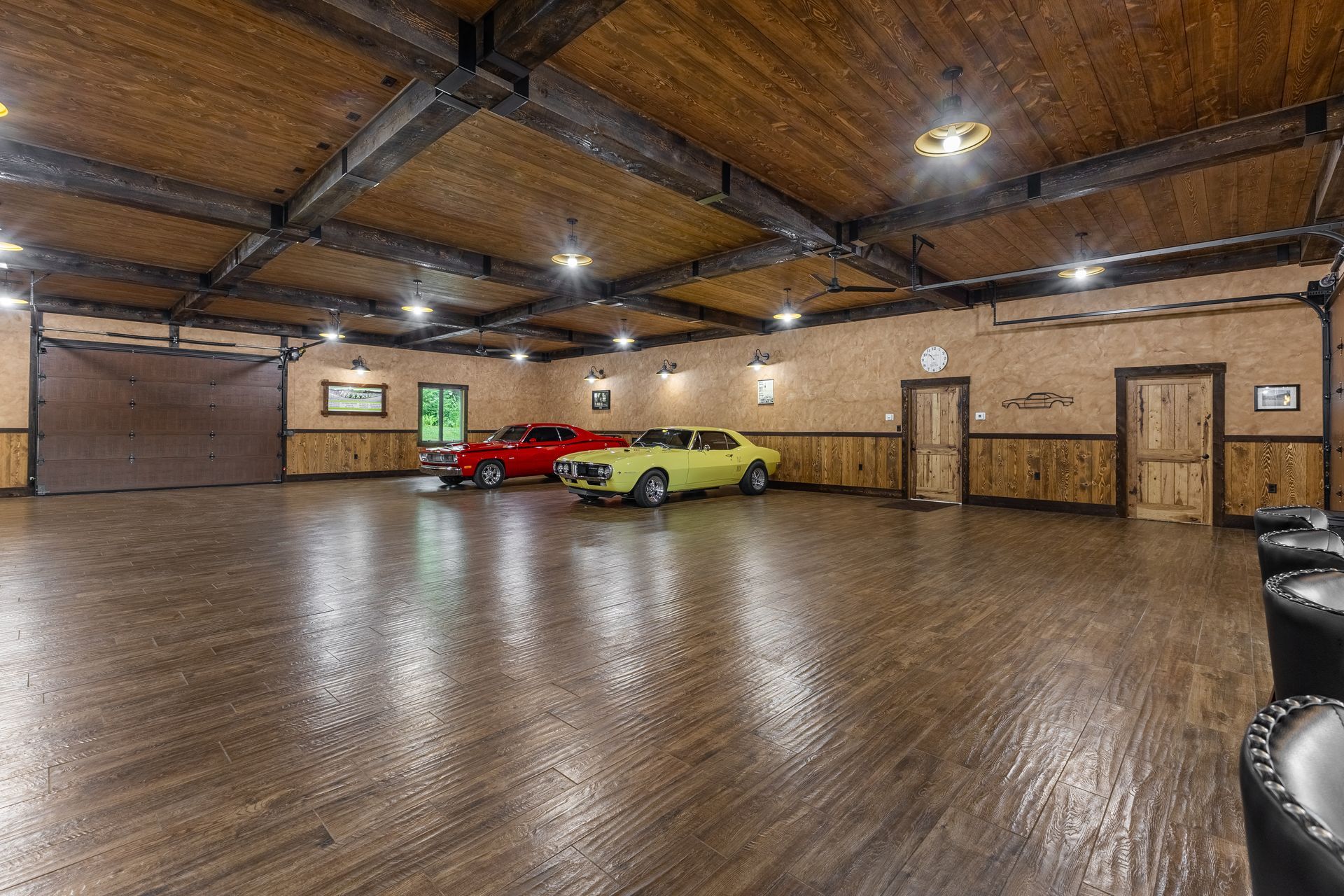 Spacious wood-paneled garage with polished floor, two parked cars, and overhead lights.