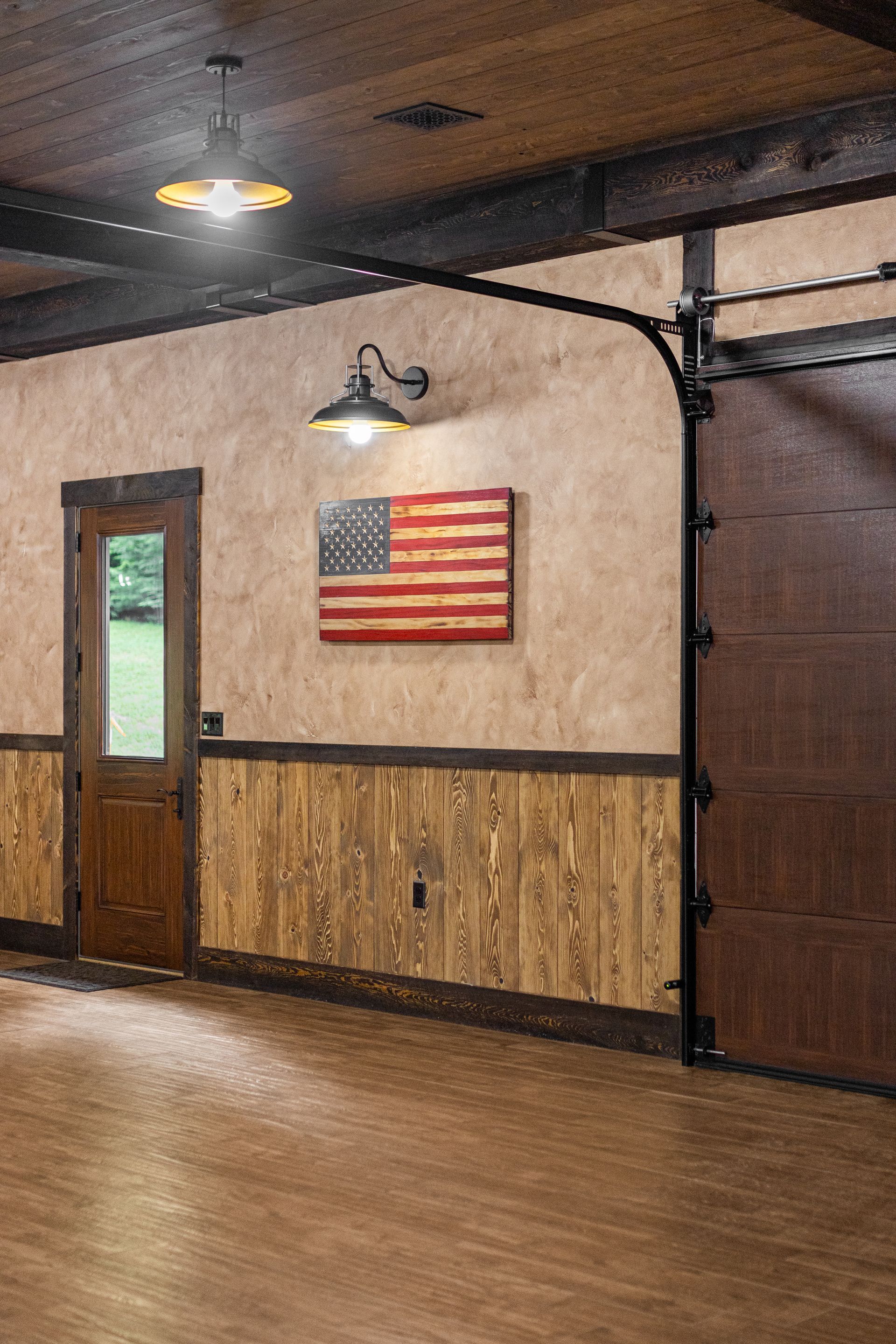 Rustic hall with wood floors, beige walls, an American flag, a door, and a large garage-style door