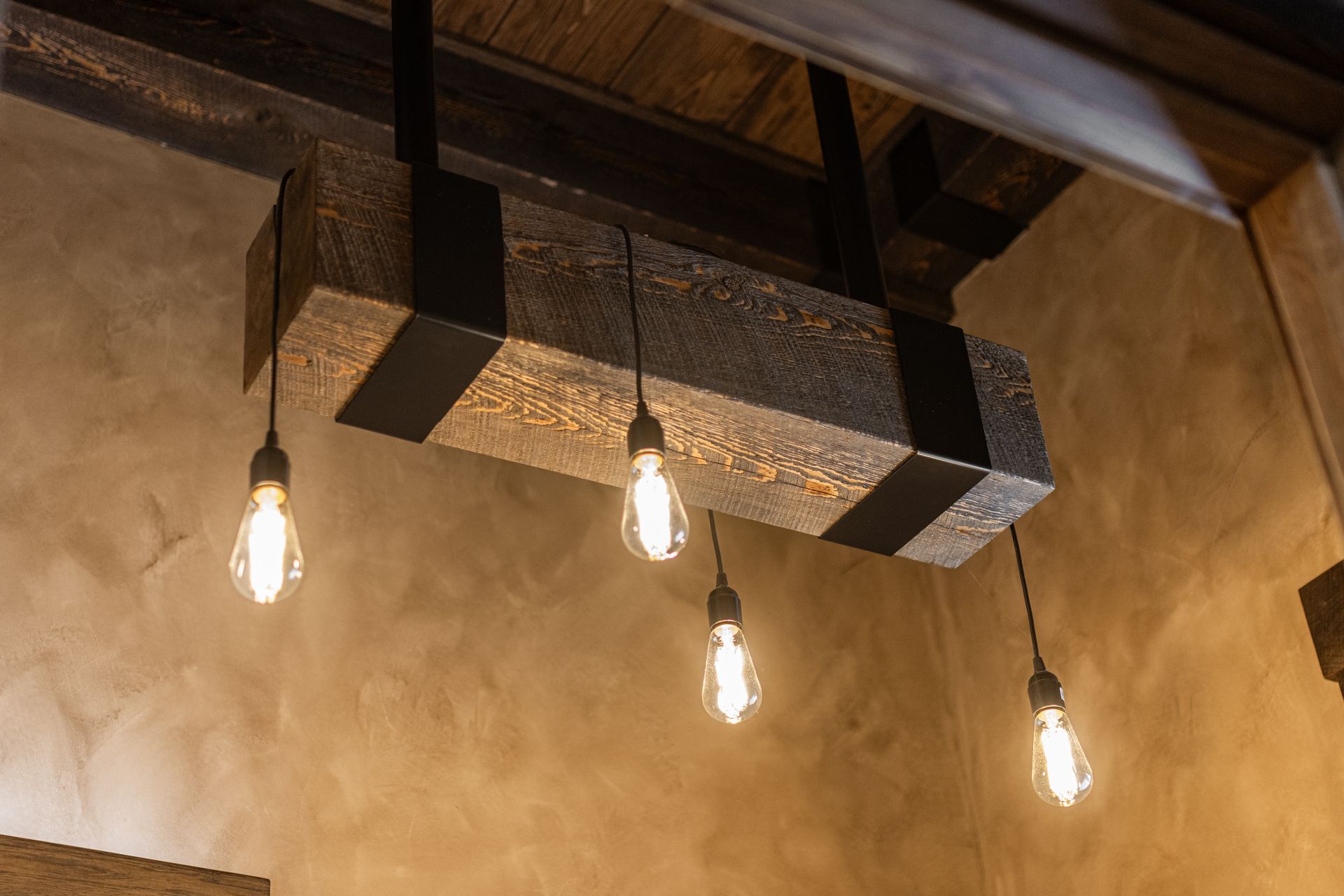 Industrial-style ceiling light fixture with four hanging Edison bulbs against a textured beige wall
