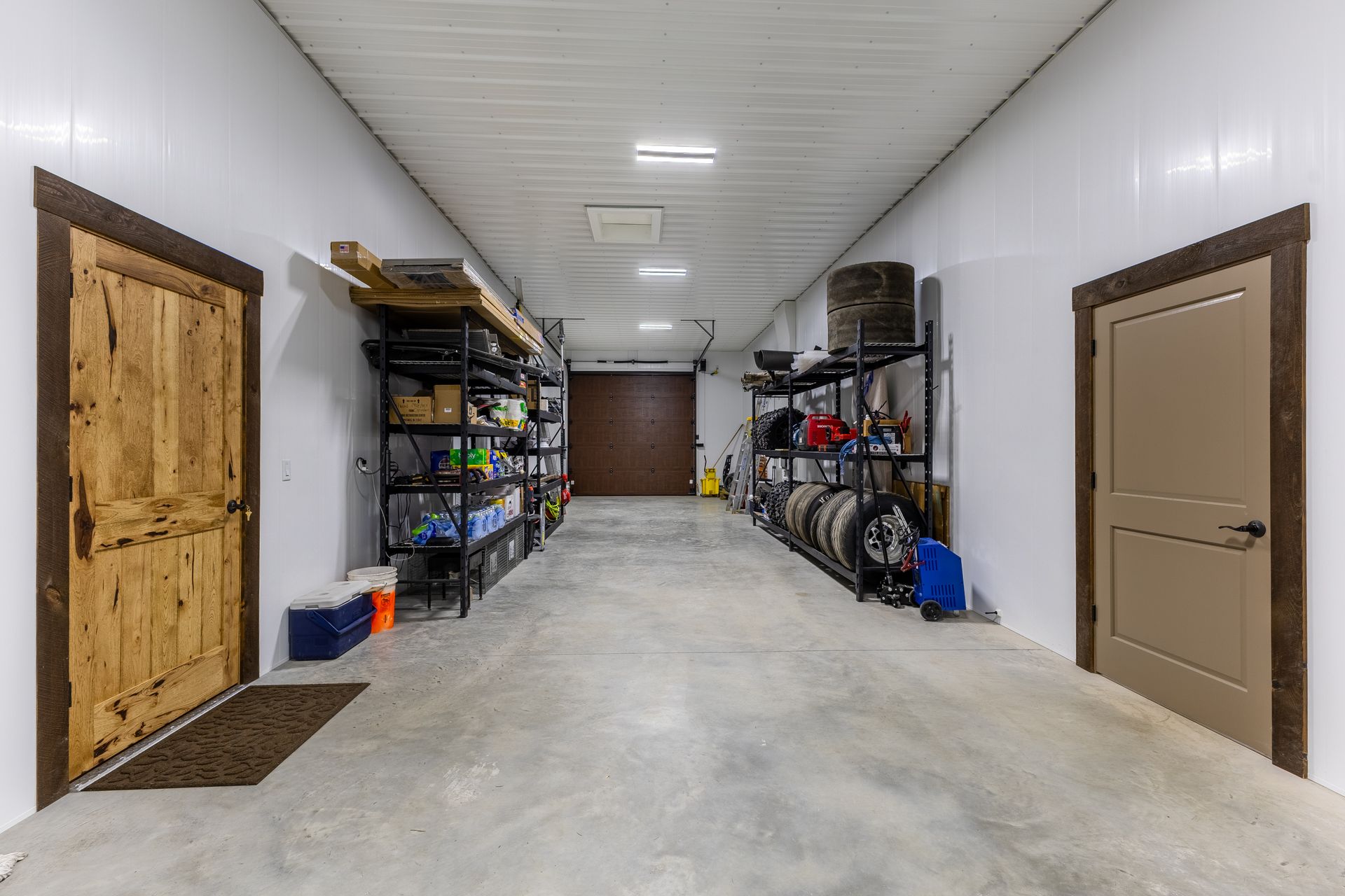 Storage room with concrete floor, white walls, metal shelving, and brown doors on both sides