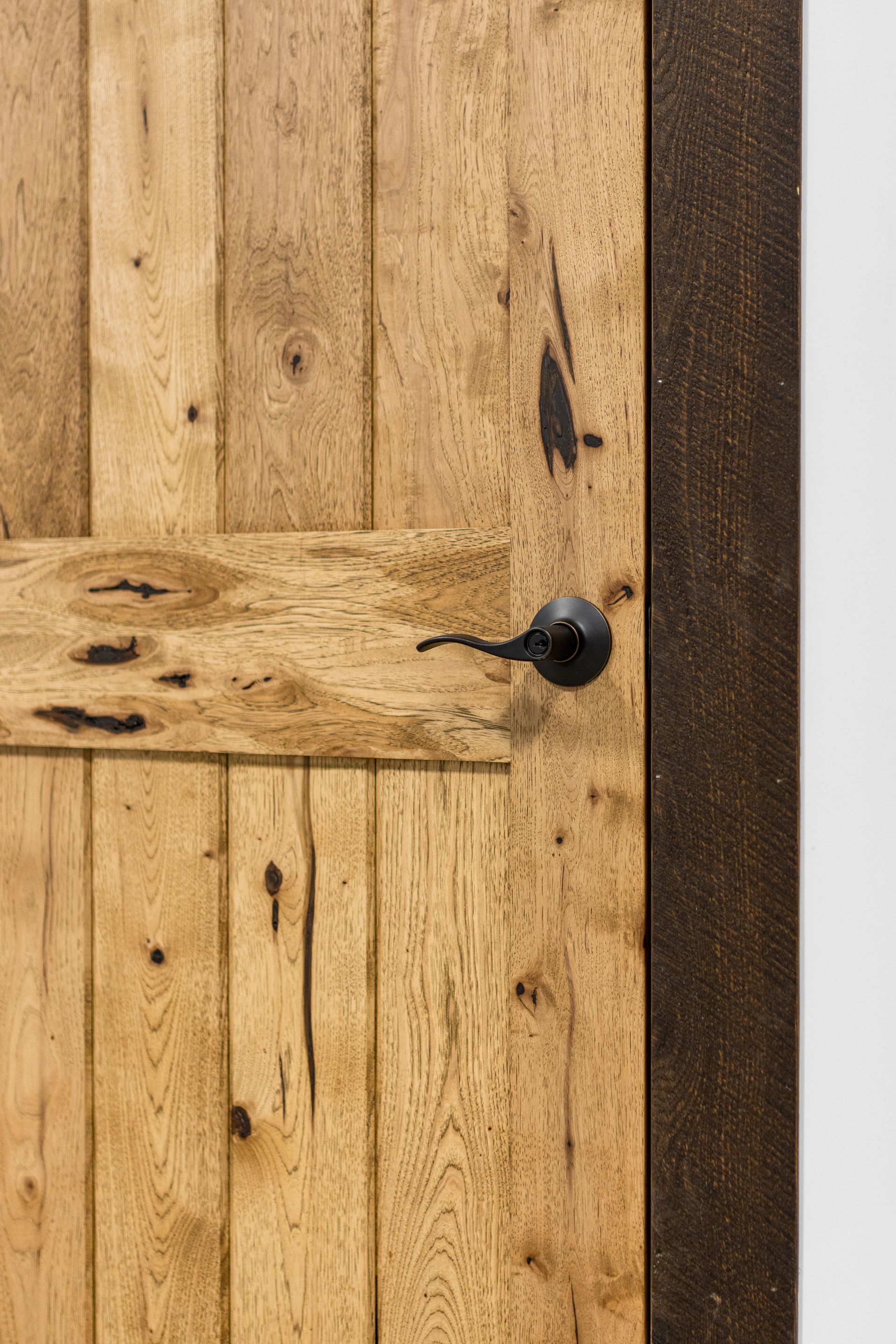 Rustic wooden door with a black handle and textured dark trim on the right