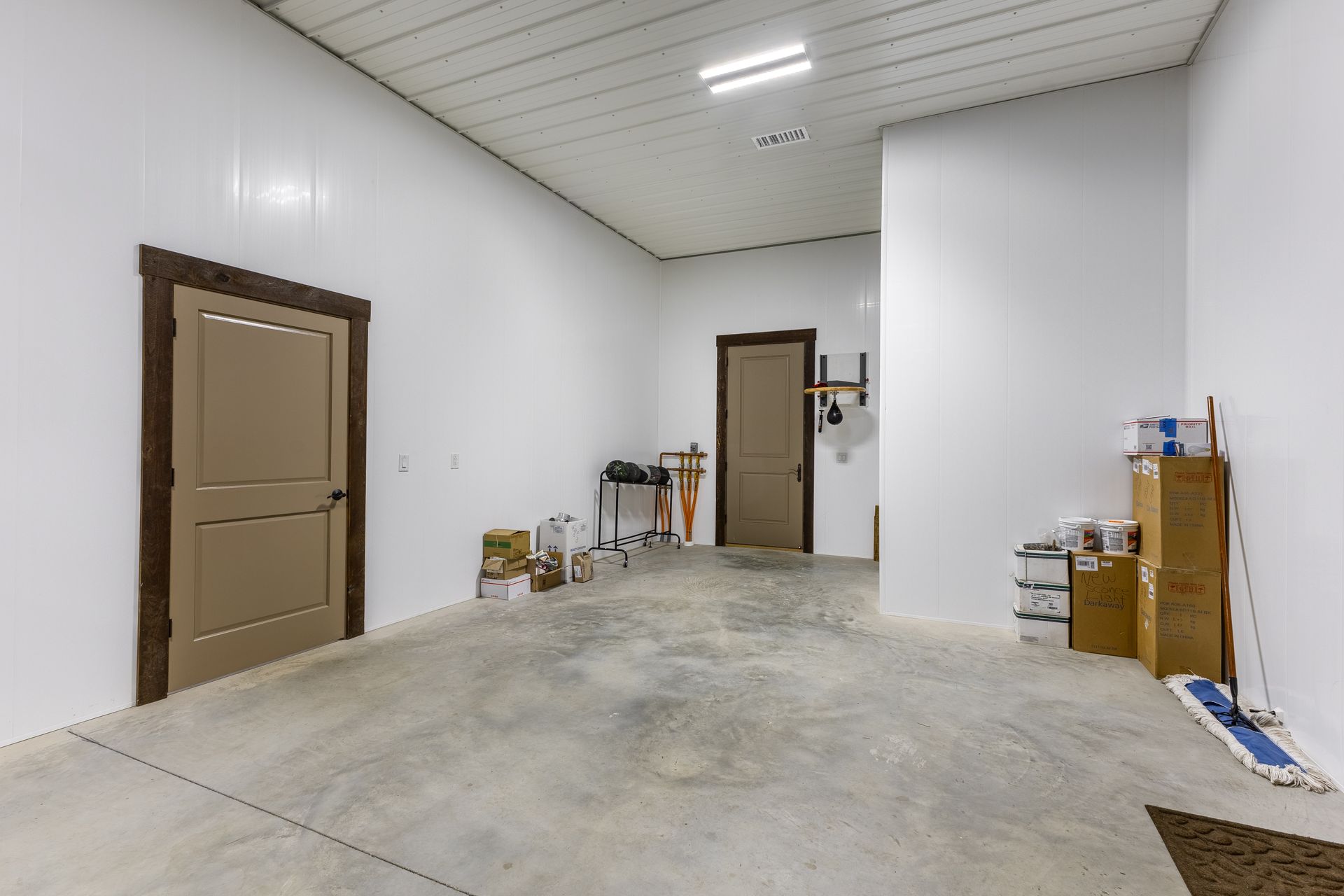 Empty industrial room with white walls, concrete floor, and a few stacked boxes and tools near the doors