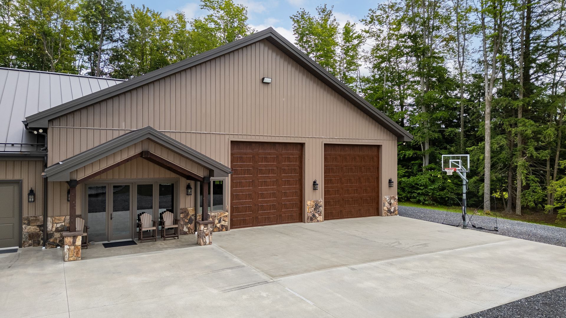 Two-car garage with beige siding, covered porch, and basketball hoop on a concrete driveway.