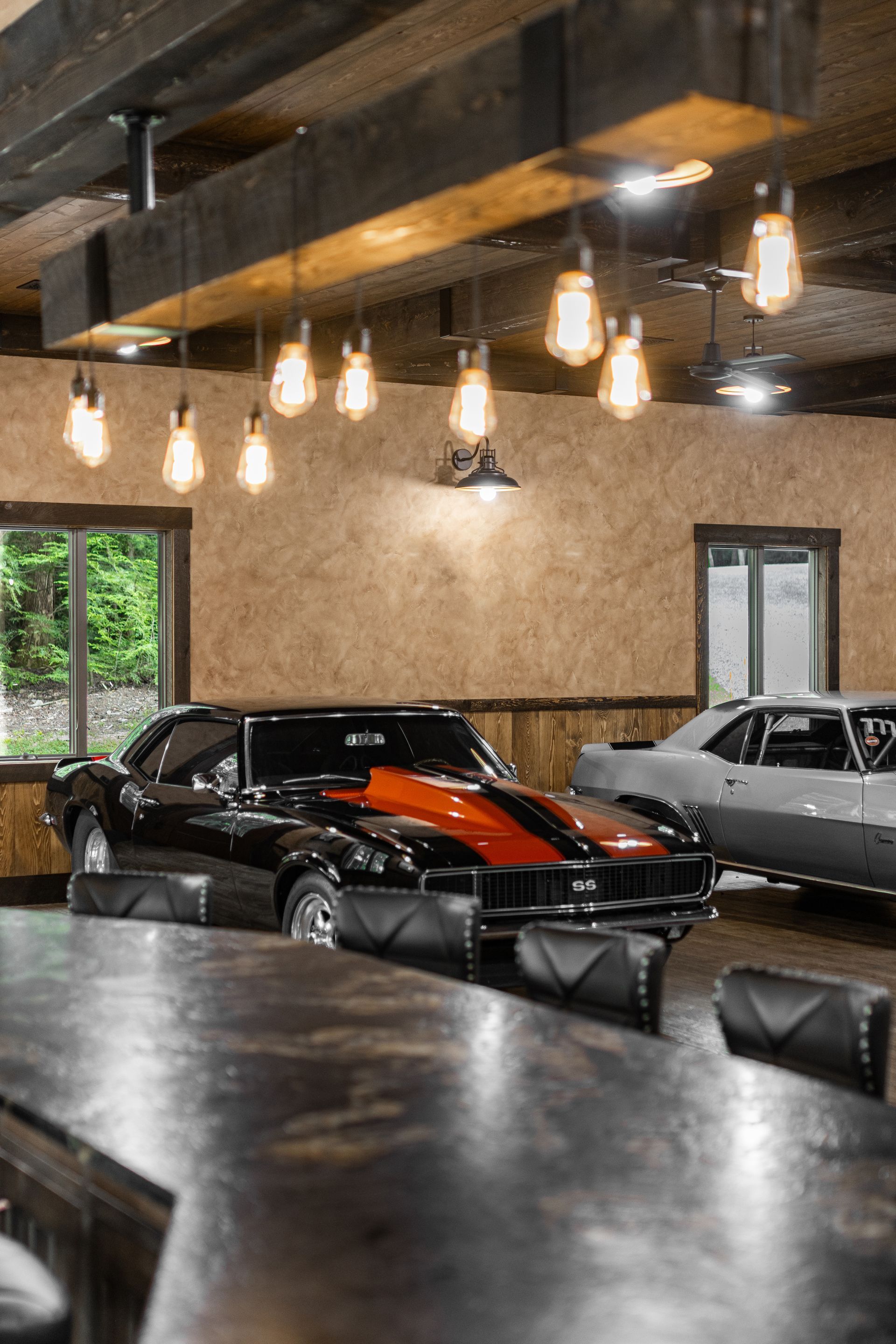Classic car display in an industrial-style garage with hanging lights and a black car with an orange stripe.
