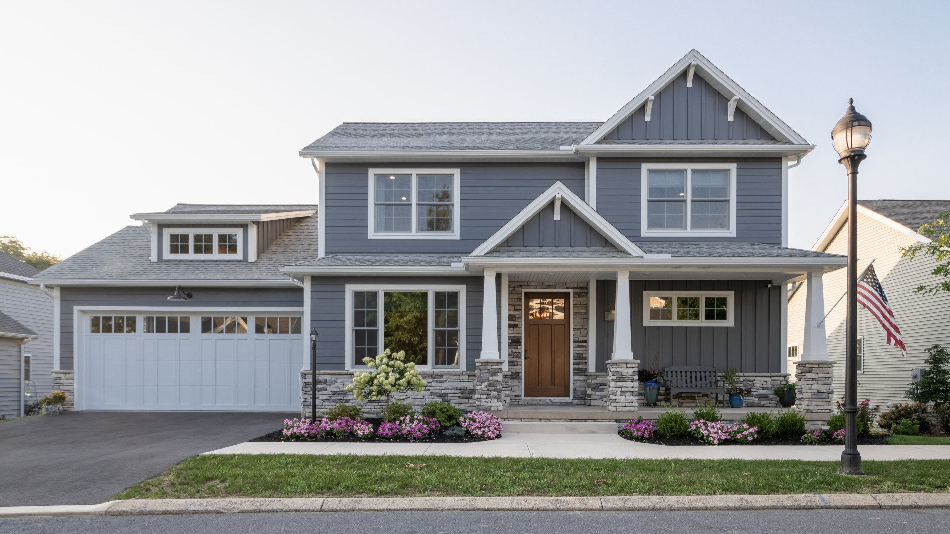 Two-story gray house with white trim, front porch, garage, and flower beds at dusk