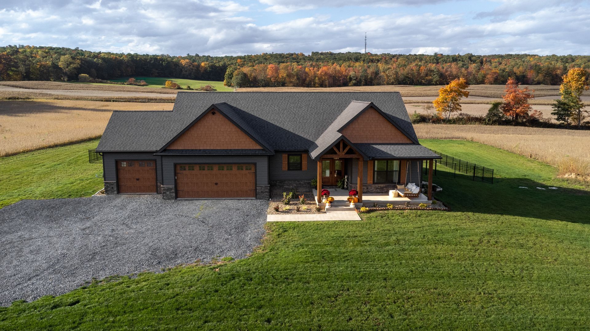 Single-story dark gray house with garage and porch, surrounded by green lawn and fall trees