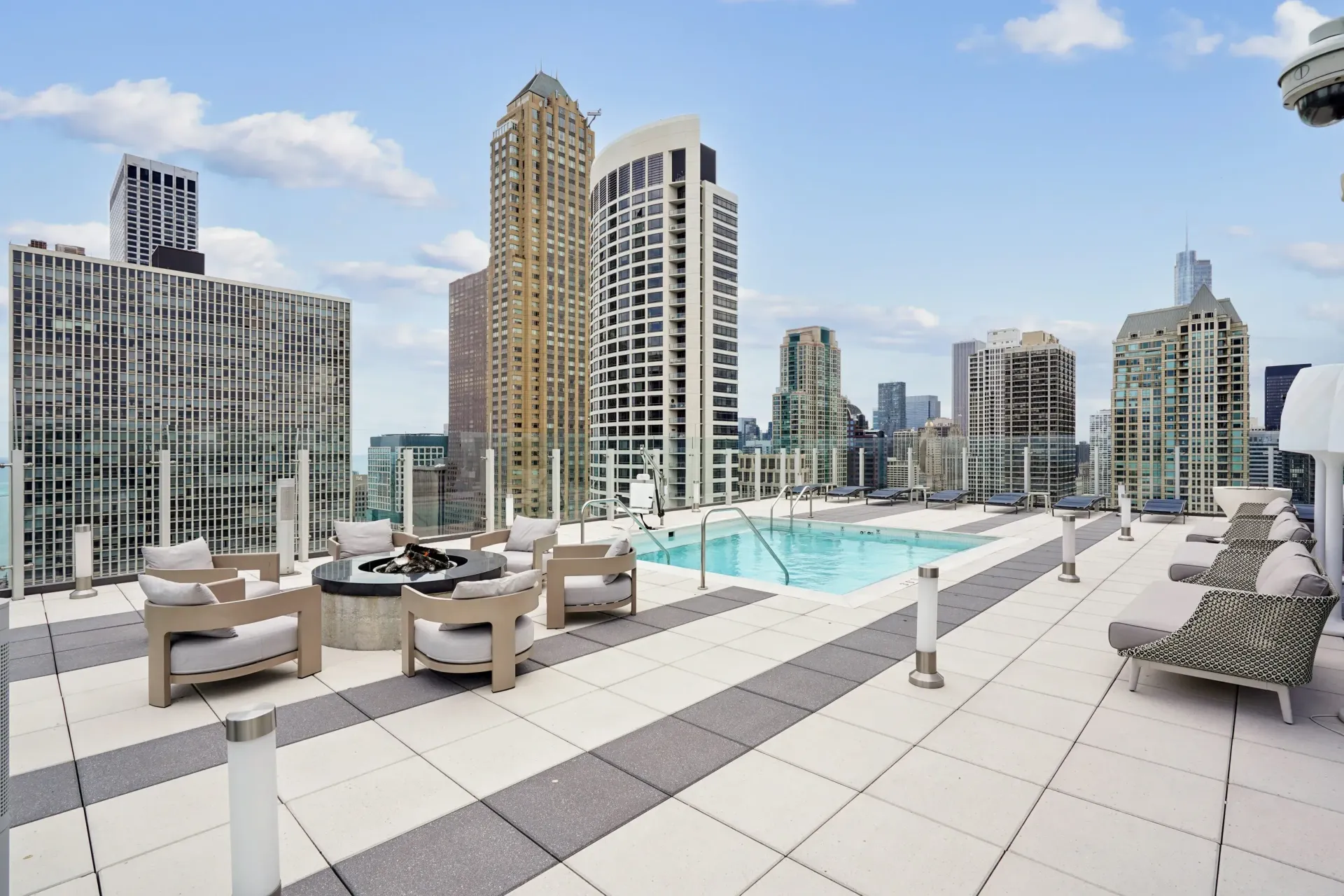 Rooftop pool lounge with city skyline, tan seating, and blue sky on a sunny day