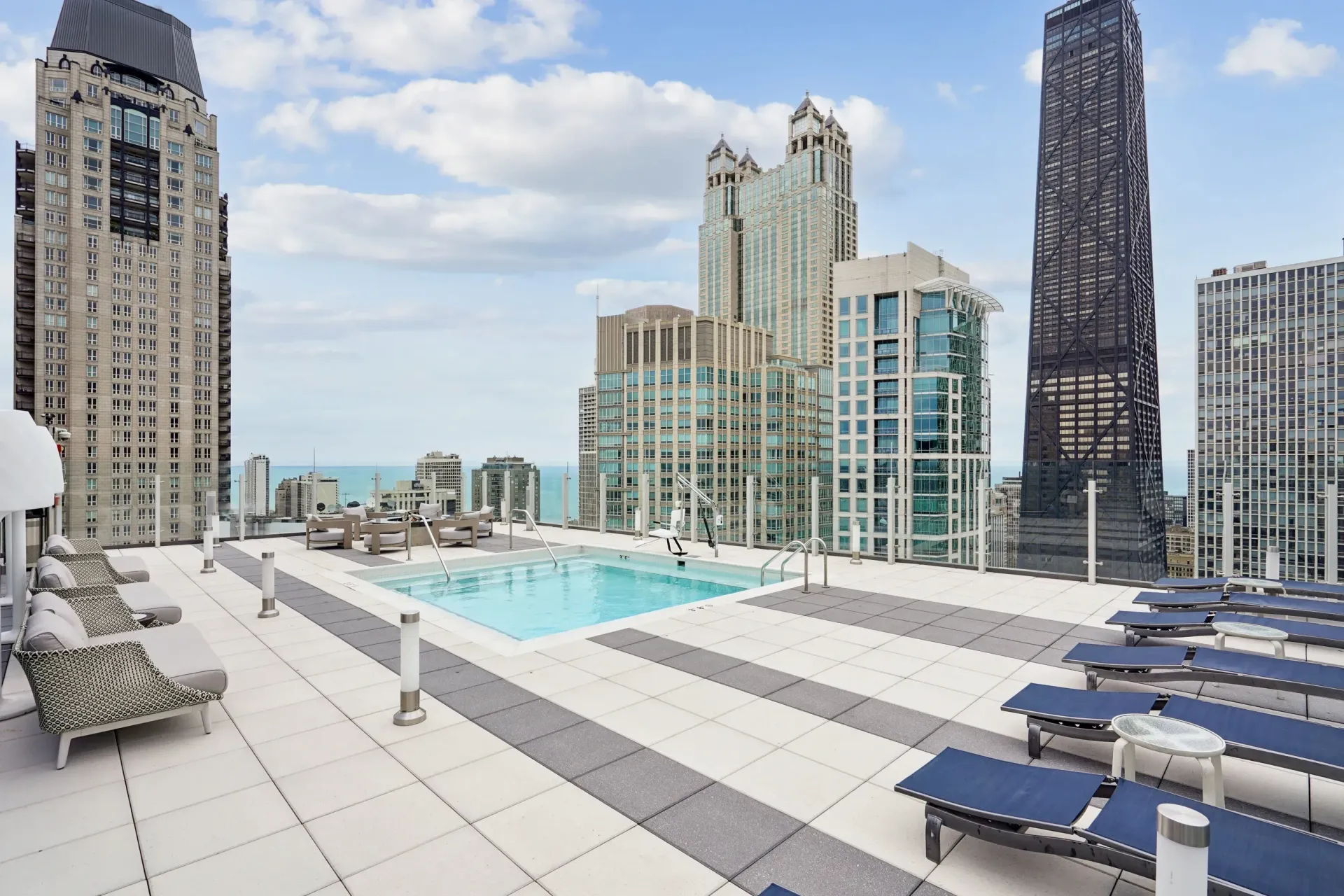 Rooftop pool terrace with lounge chairs and city skyline under a partly cloudy sky